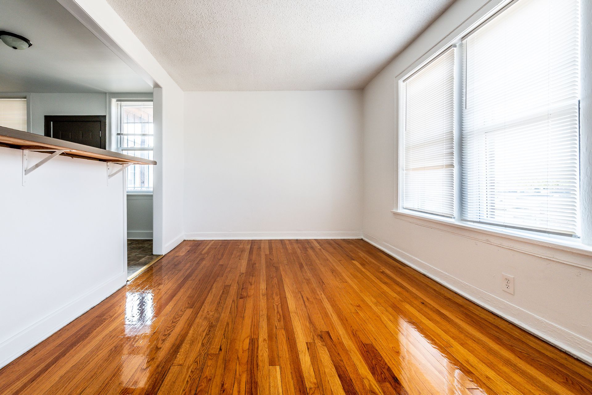 Empty room with hardwood floors, white walls, and a large window with blinds.