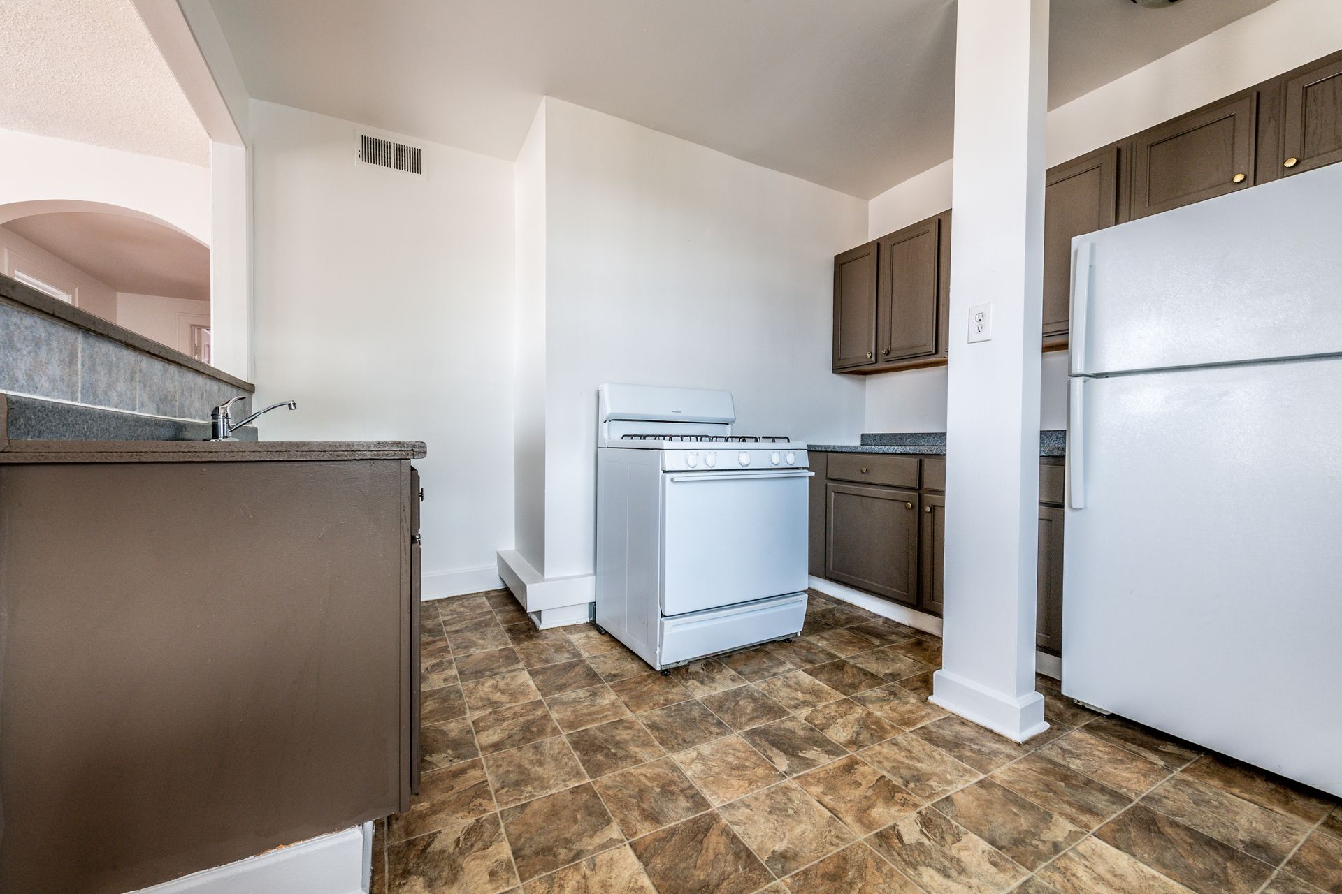 A kitchen with a white stove, refrigerator, brown cabinets, and patterned flooring.