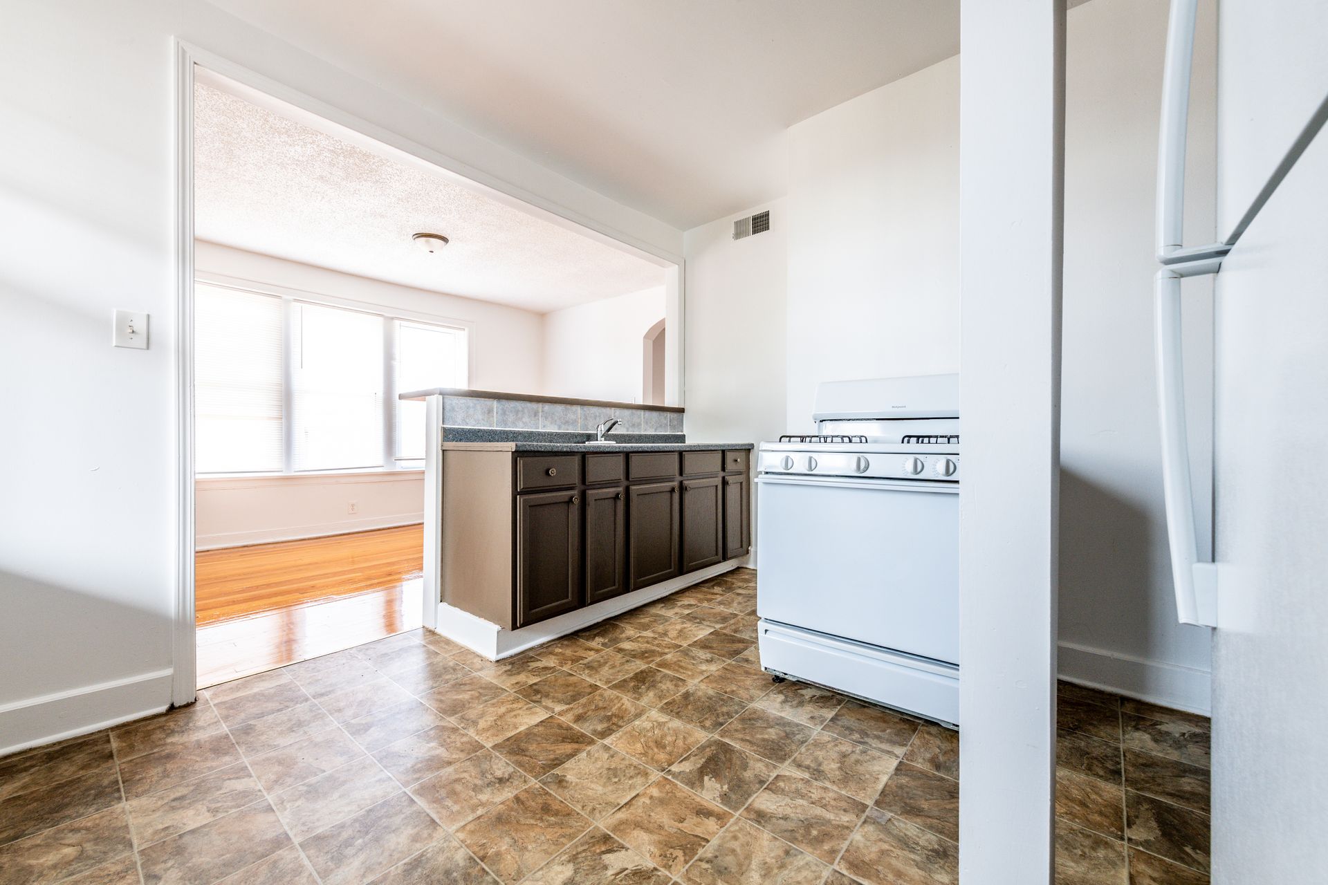 Kitchen with dark brown cabinets, white stove, and view into a room with windows and wood flooring.