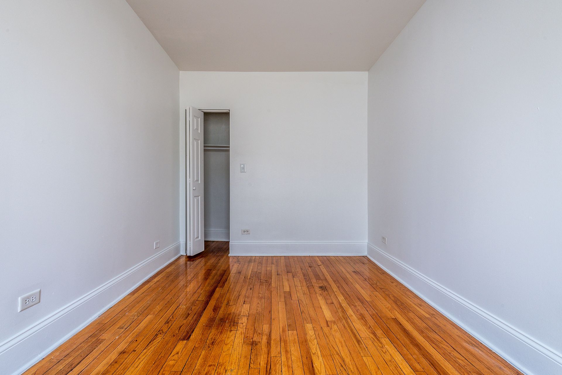 Empty room with hardwood floors, white walls, and an open closet.