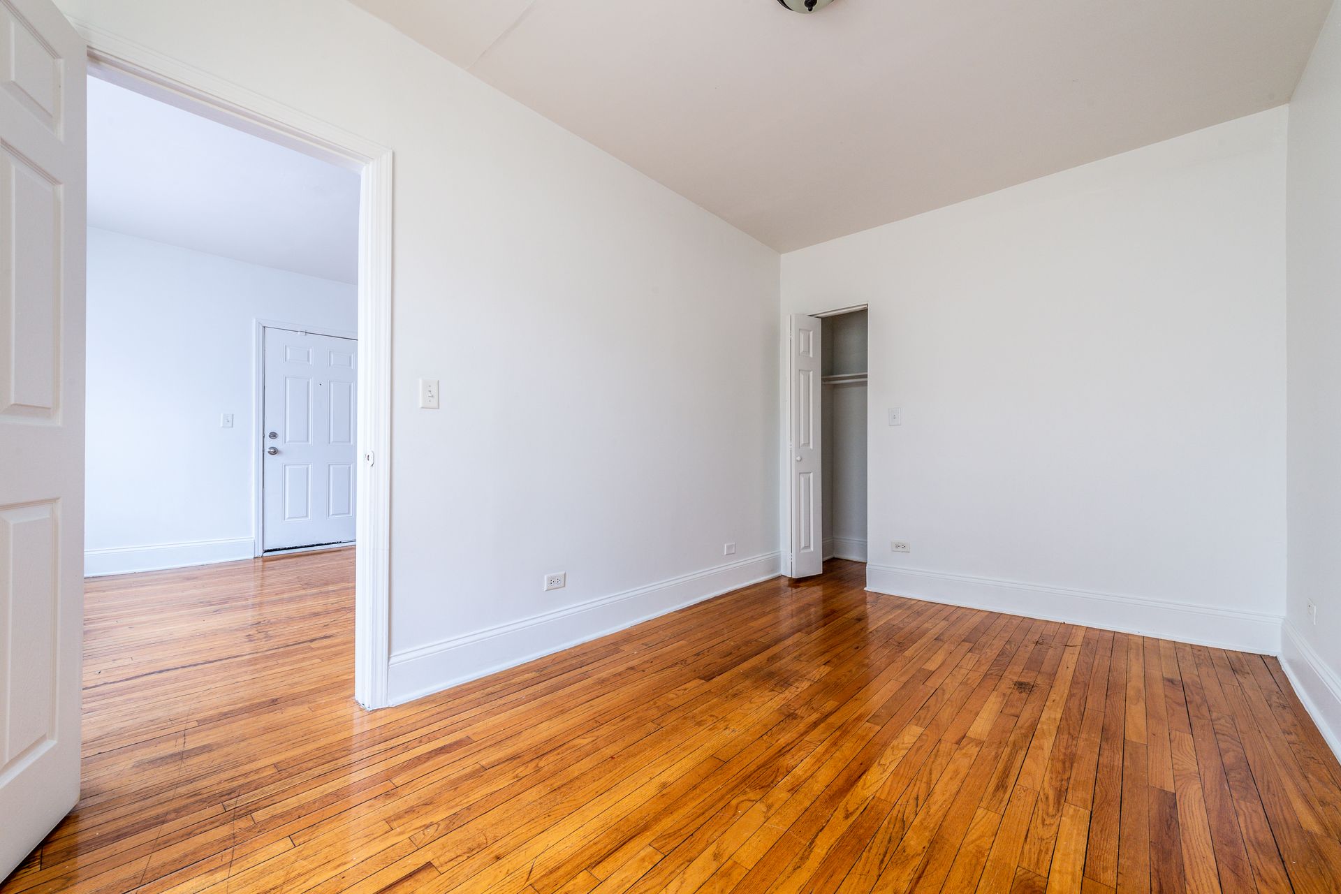 Empty room with hardwood floors, white walls, and an open doorway.