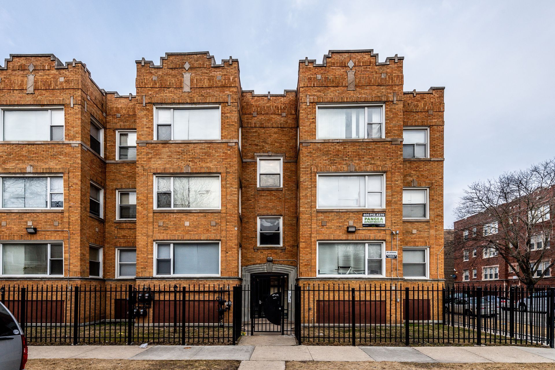 Three-story brick apartment building with black wrought iron fence. Overcast sky.