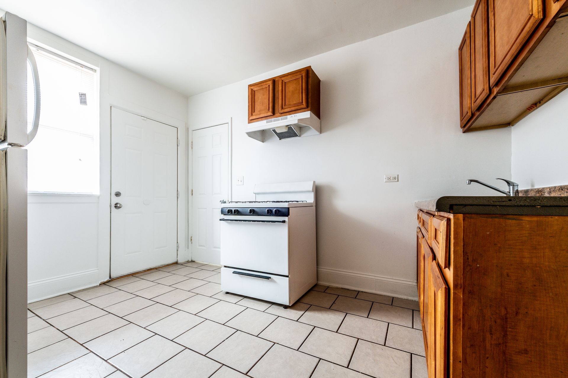 Kitchen with white appliances, brown cabinets, tile floor, and a door to the left.