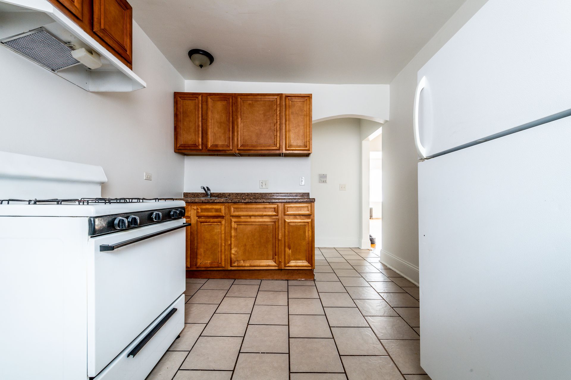 Kitchen with white appliances, brown cabinets, and tile floor.