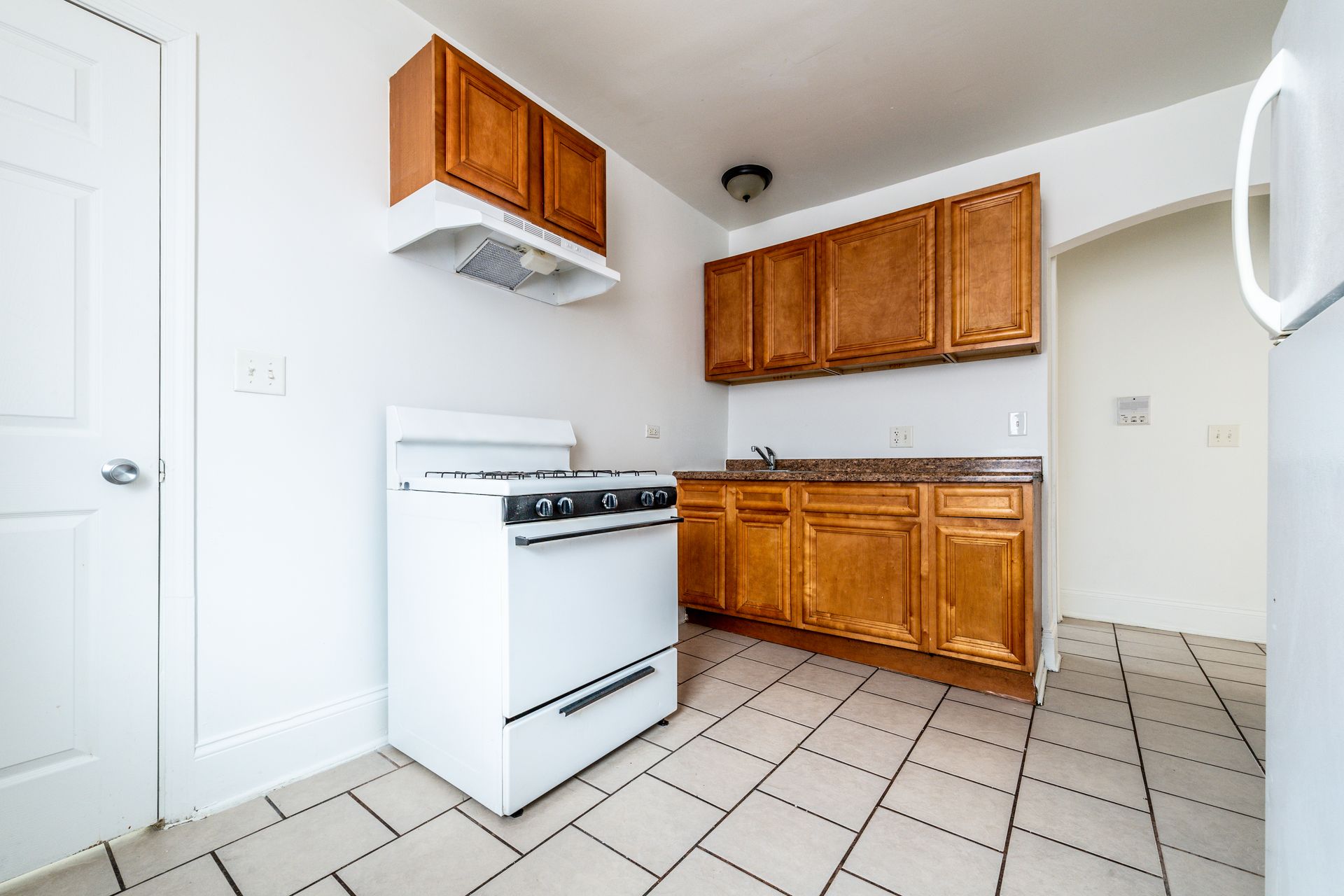 Small kitchen with wood cabinets, white appliances, and tiled floor.