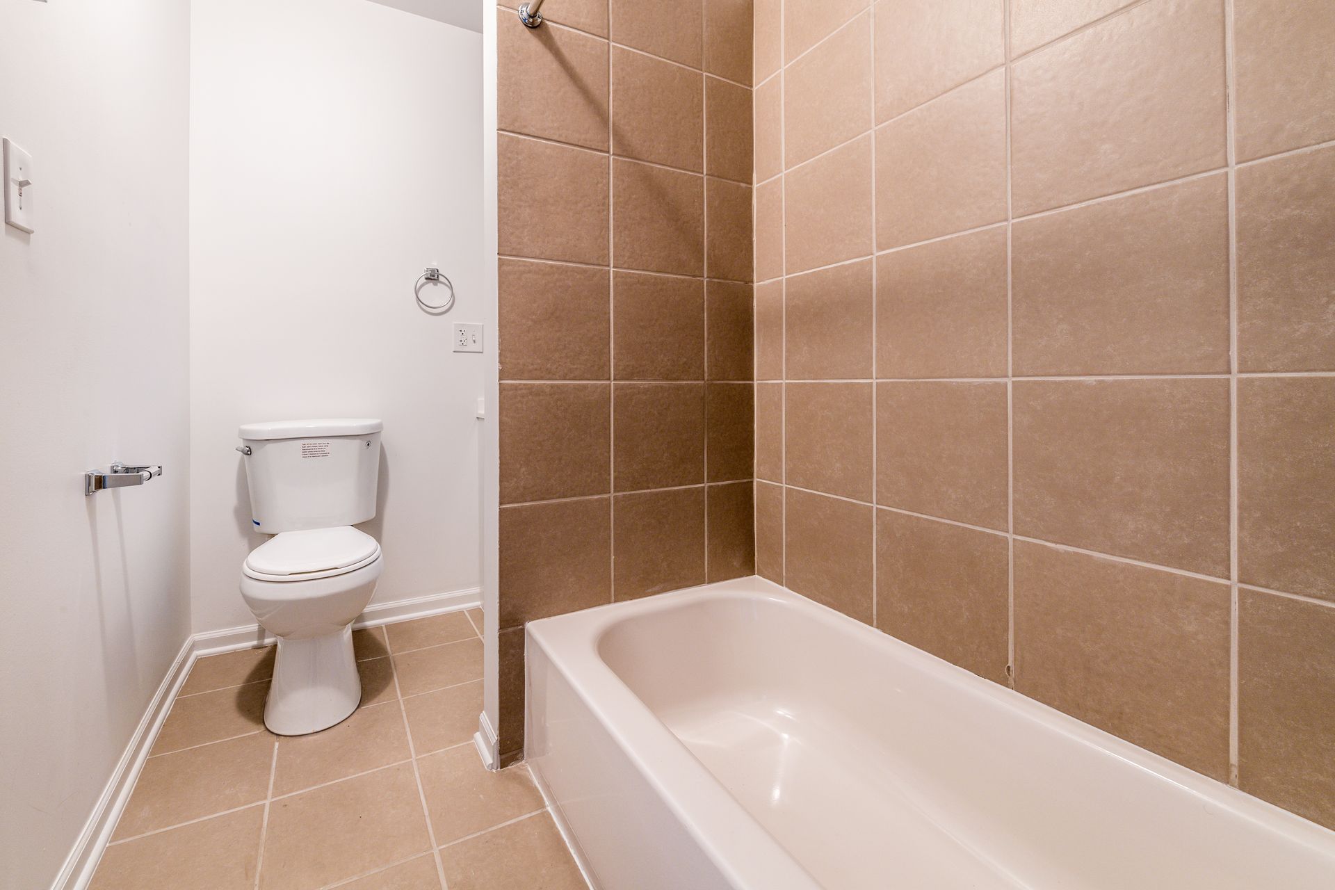 Bathroom with white toilet, bathtub, and brown tiled walls.
