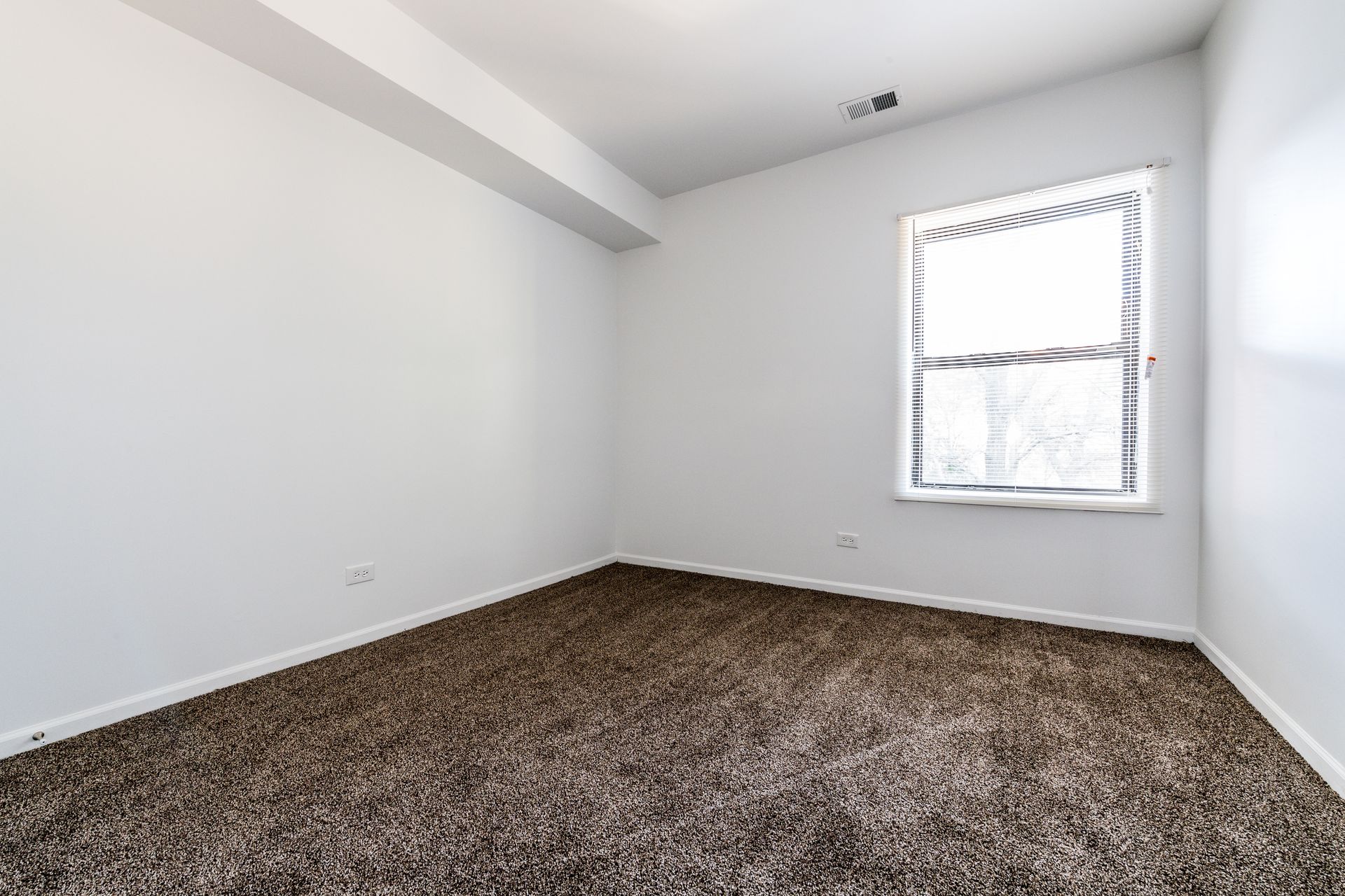 Empty room with brown carpet, white walls, and a window with blinds.