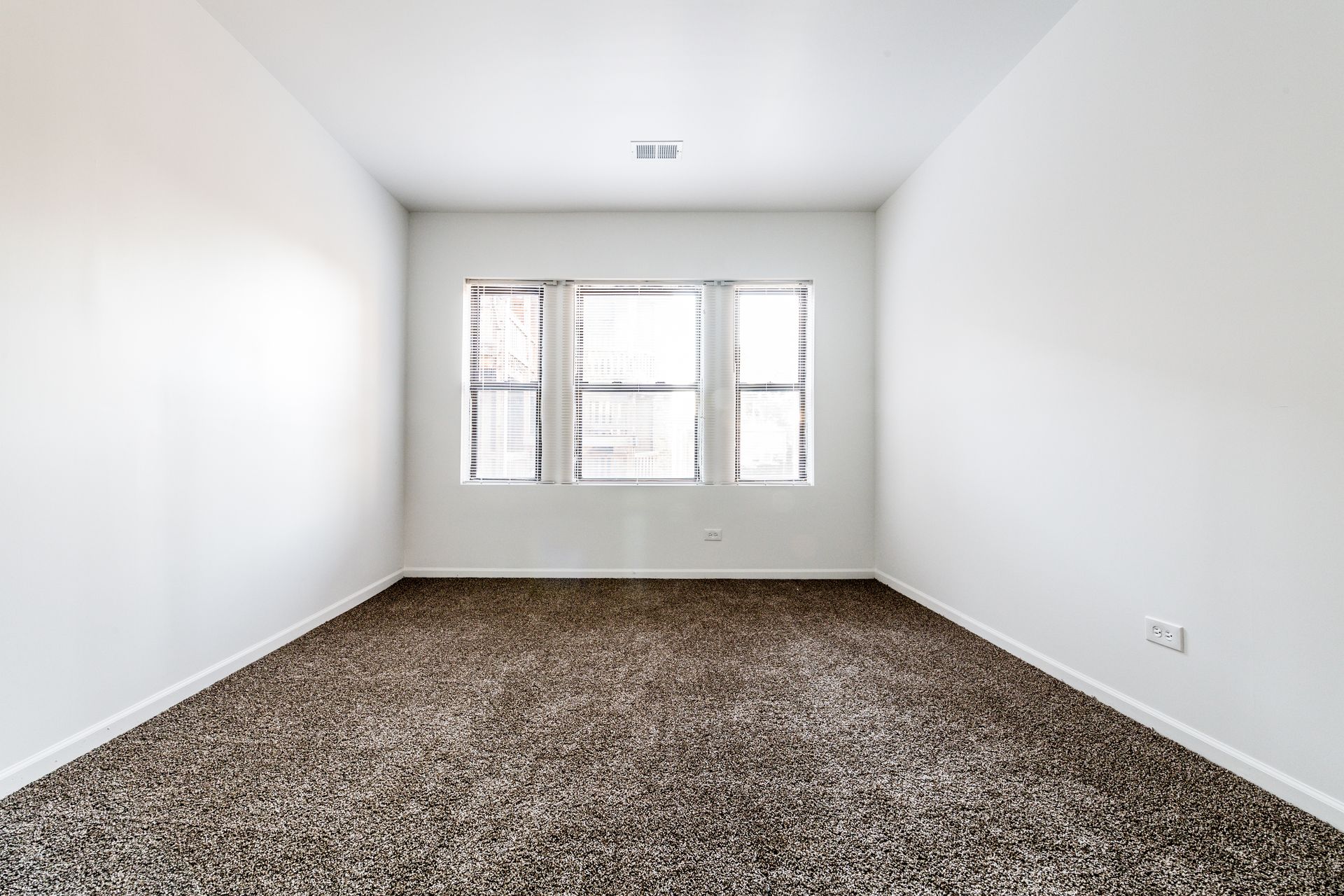 Empty room with white walls, brown carpet, and a window.