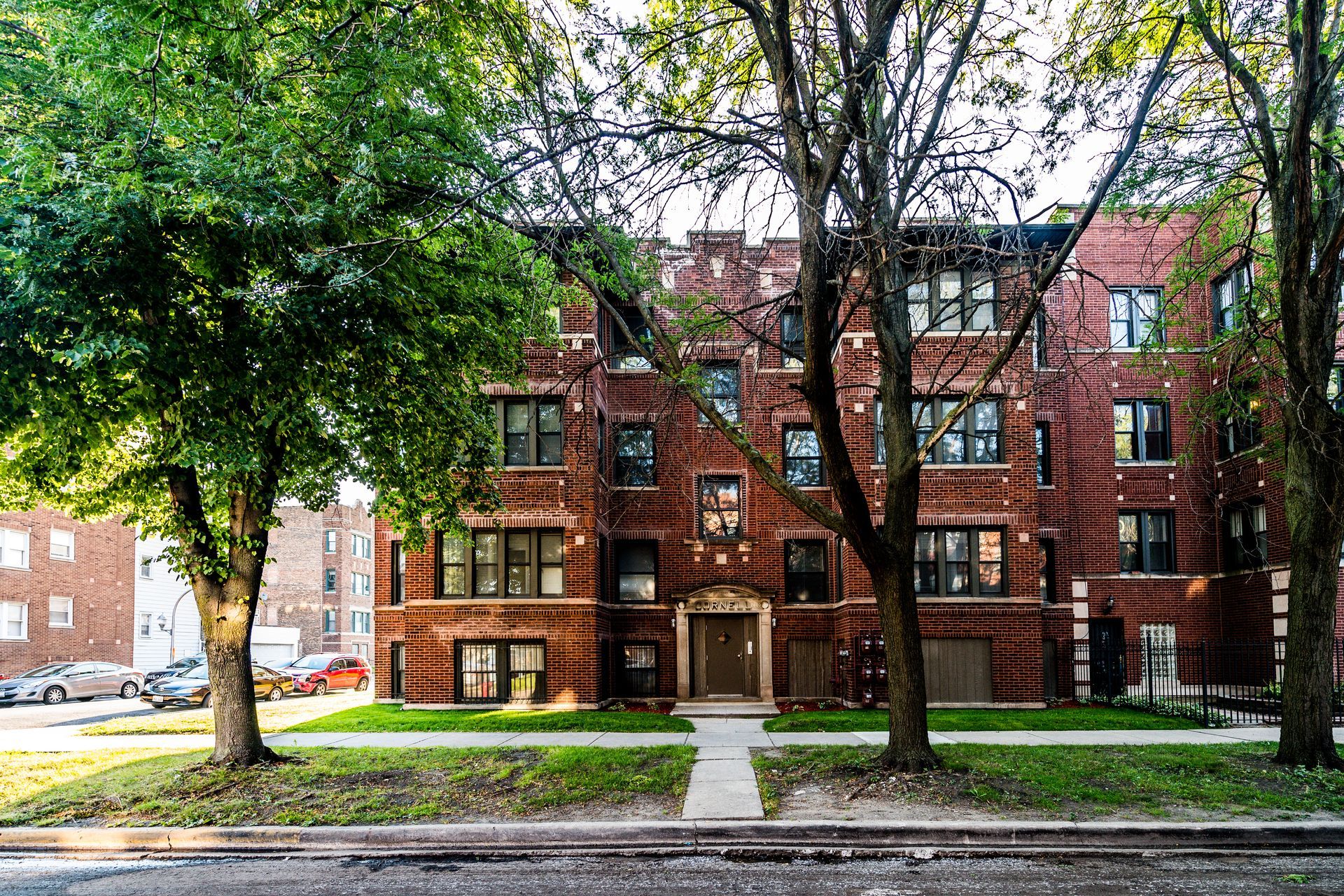 Brick apartment building with trees, green grass, and sidewalk.
