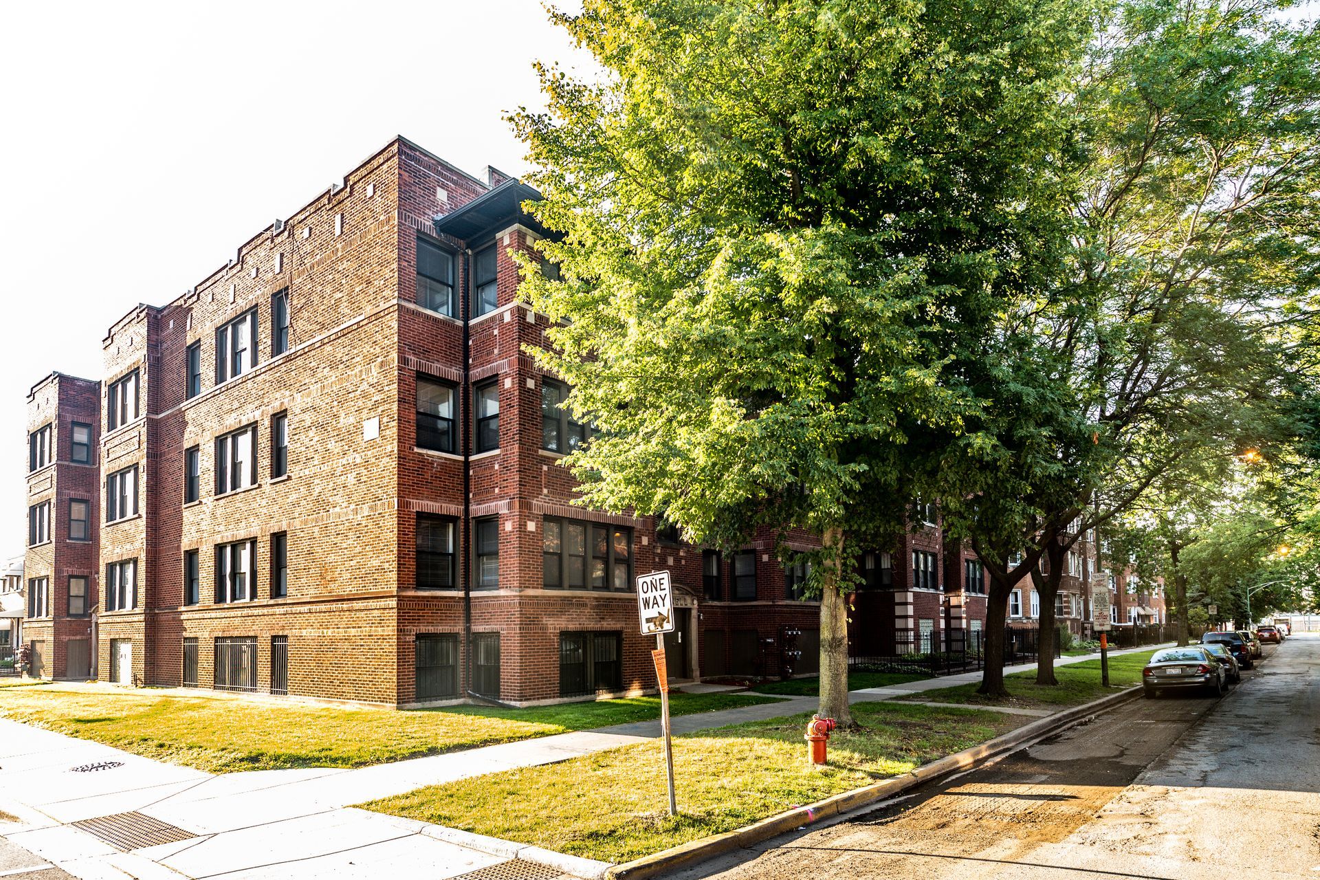 Brick apartment building with green lawn, trees, and a street.