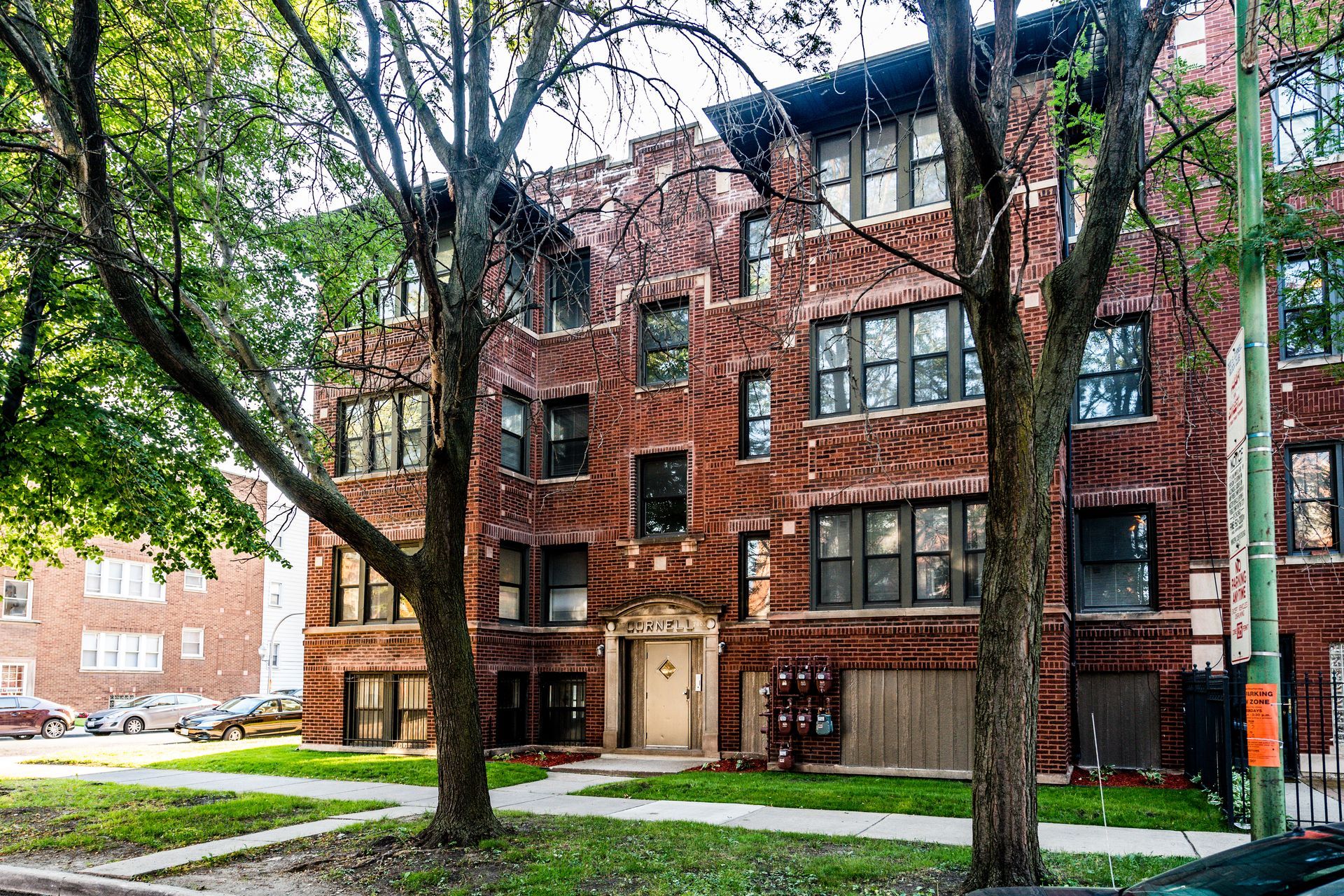 Red brick apartment building with trees in front, on a sunny day.