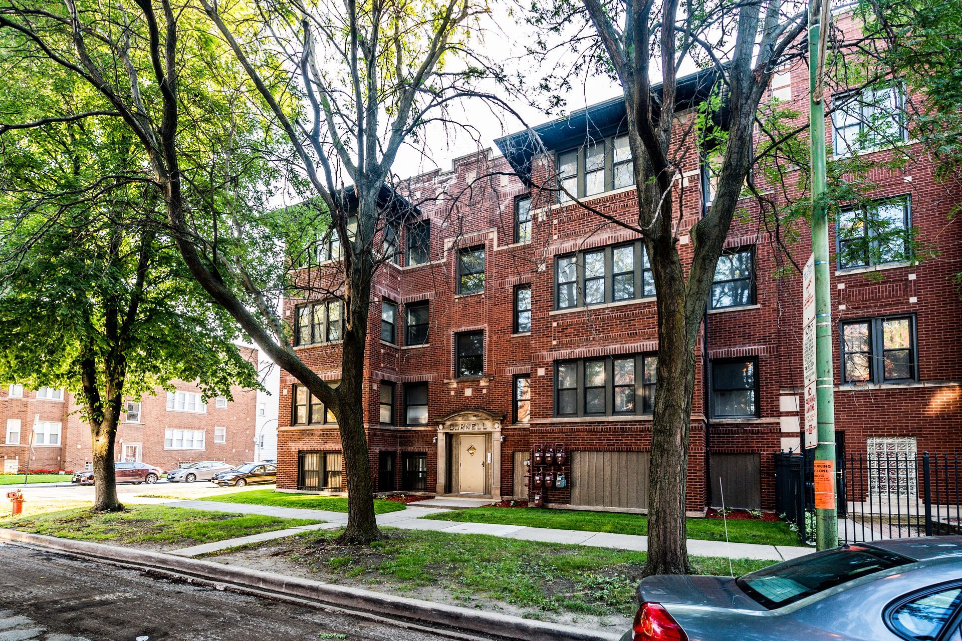 Red brick apartment building with trees in front, on a sunny day.