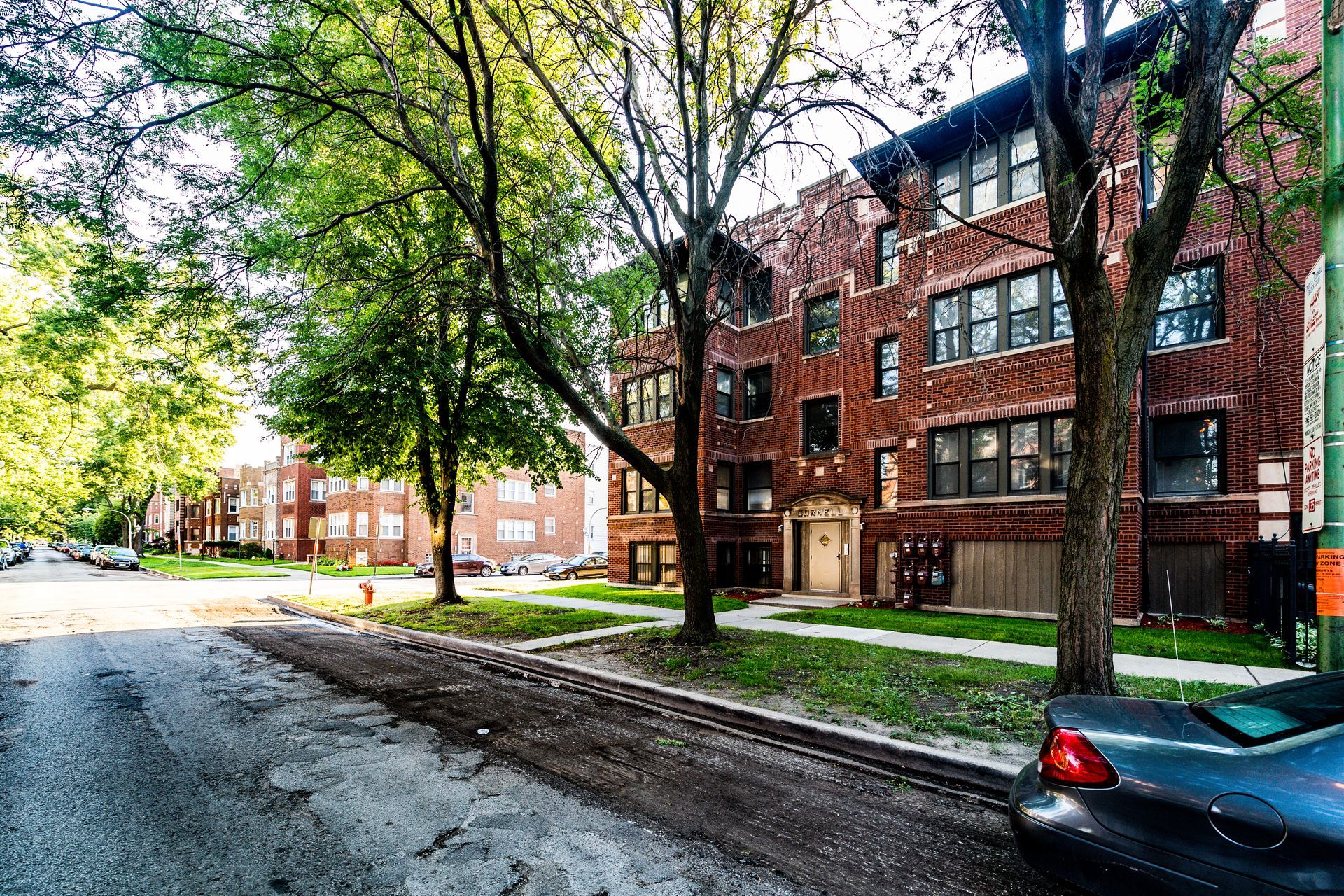 Brick apartment building on a tree-lined street with a parked car.