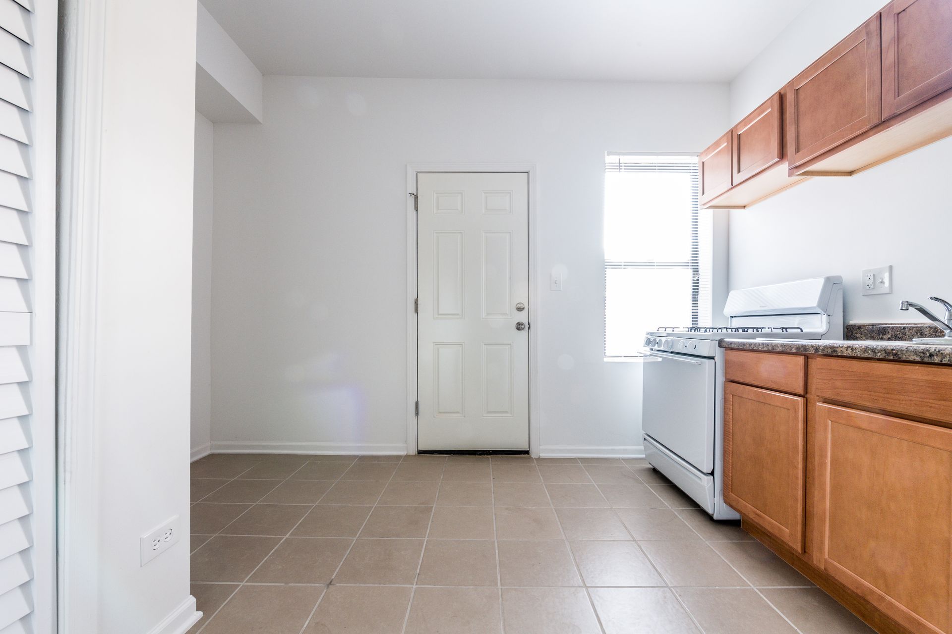 Empty kitchen with tan tile floor, white appliances, and wooden cabinets.