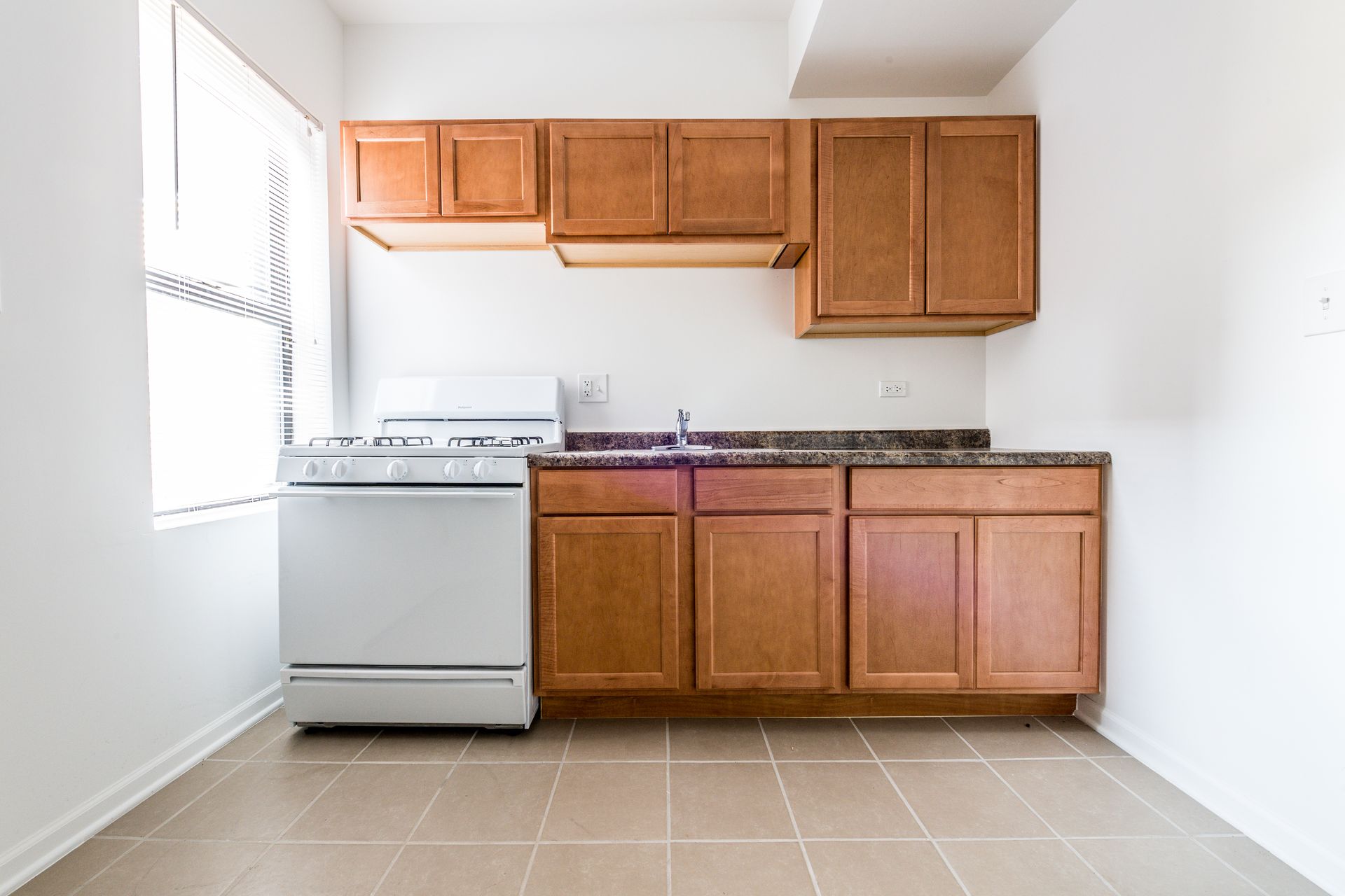 Small kitchen with wood cabinets, white stove, and window.