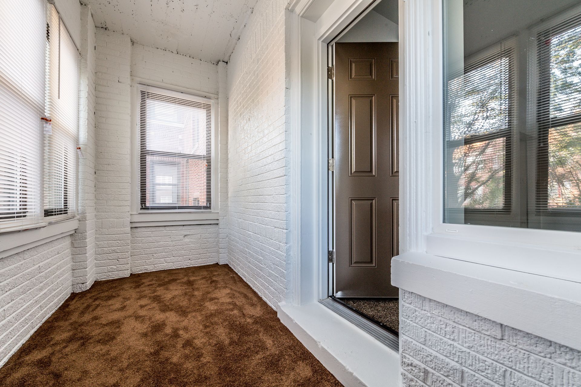 Small, white-painted room with brown carpet, windows, and a brown door.
