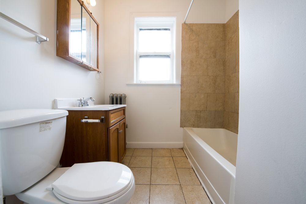 Bathroom with toilet, sink, and bathtub. Beige tiles and walls, with a small window.