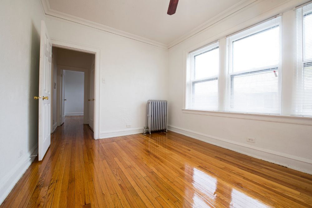 Empty room with hardwood floors, a radiator, and large windows.