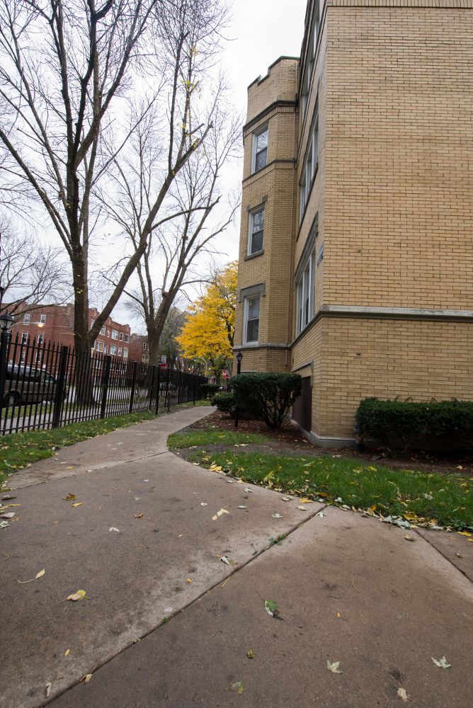 Sidewalk curves along a brick building with trees on a cloudy day.