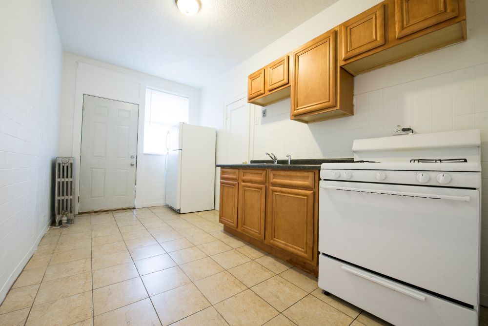 Empty kitchen with wooden cabinets, white appliances, and tiled floor.