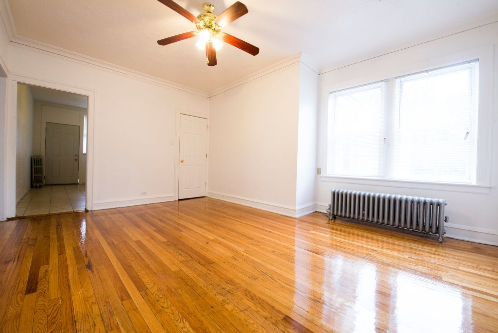 Empty room with hardwood floors, a radiator, windows, and a ceiling fan.