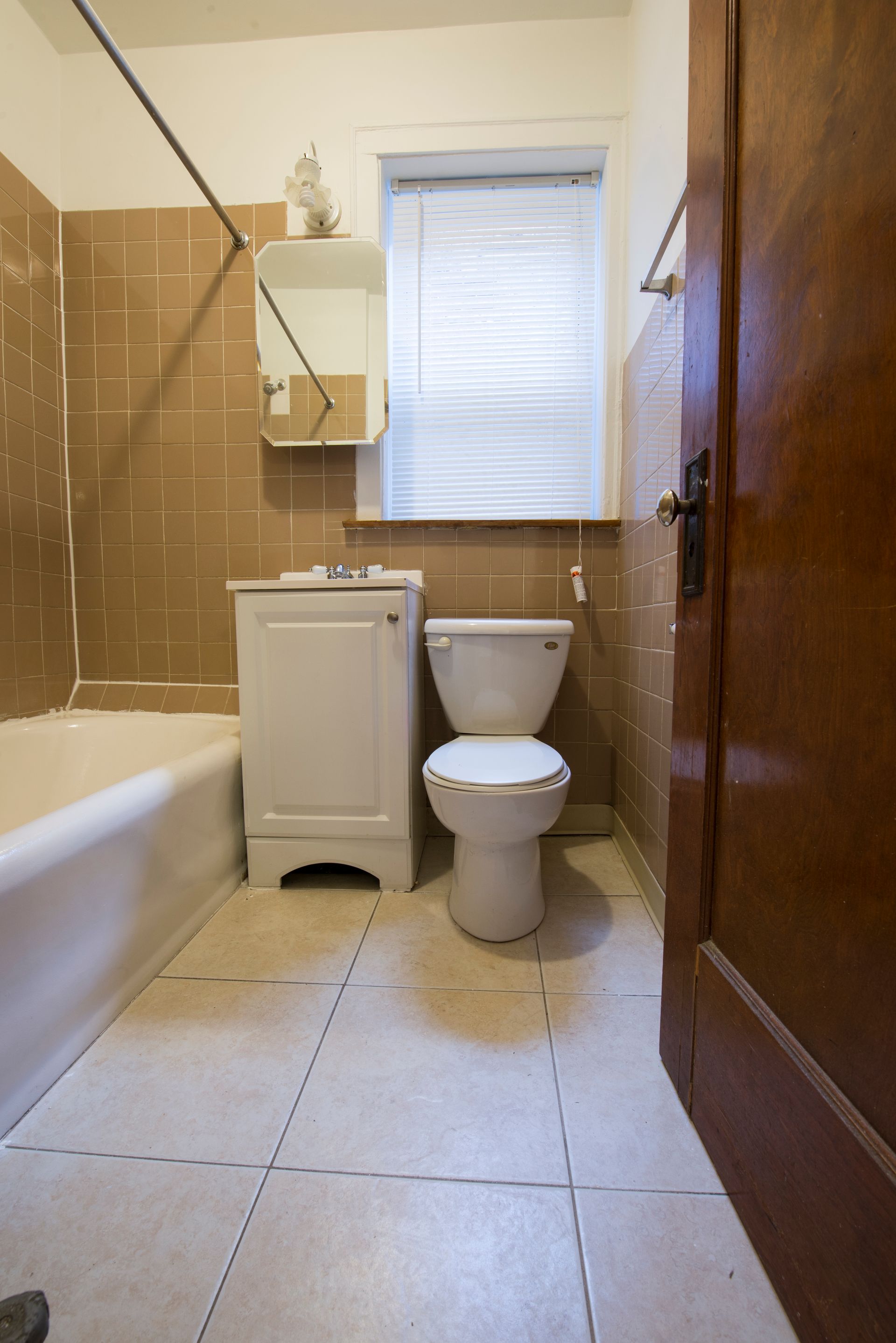 Small bathroom with beige tile, white toilet and sink, and a closed wooden door.