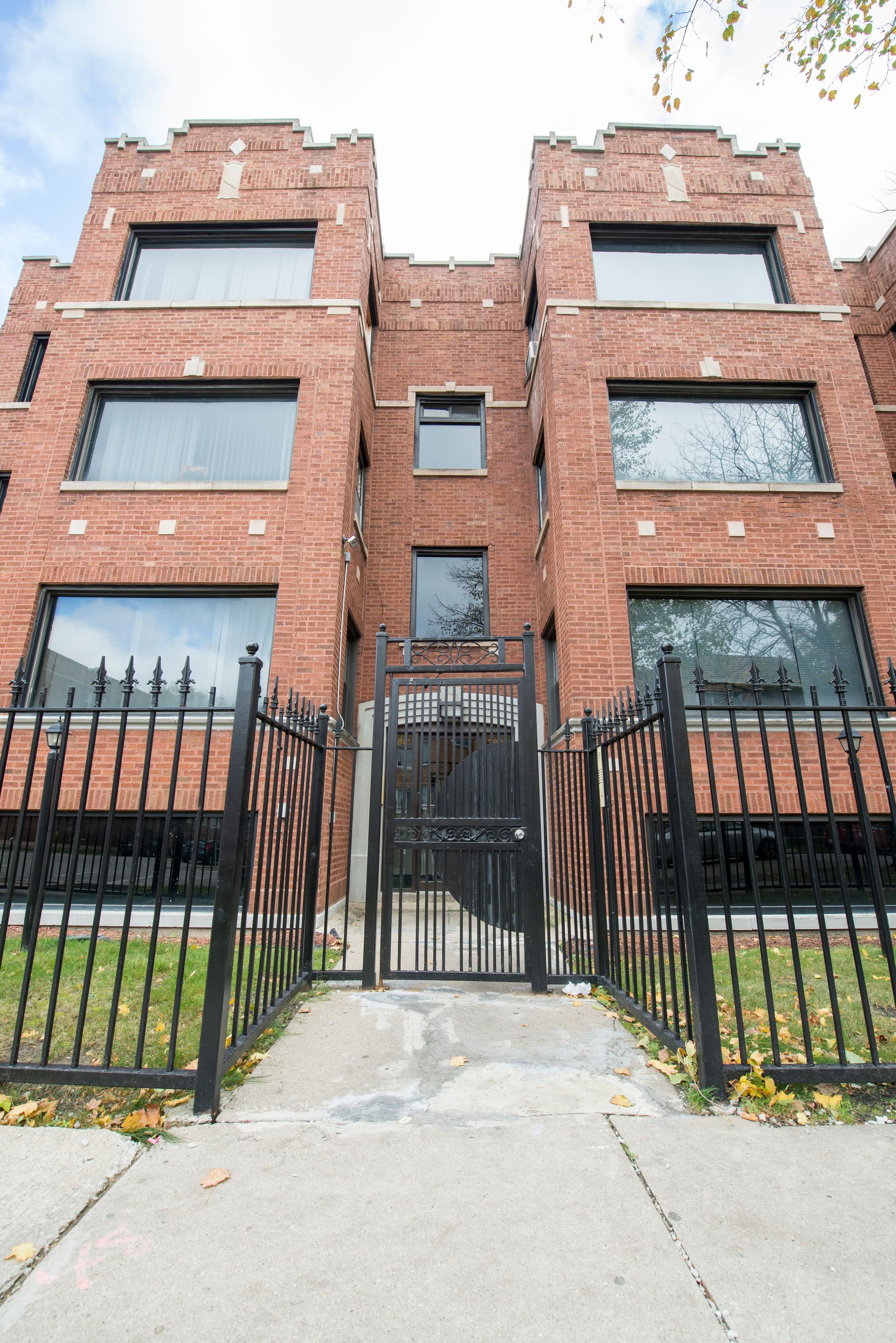 Brick building with large windows behind a black metal fence and gate.