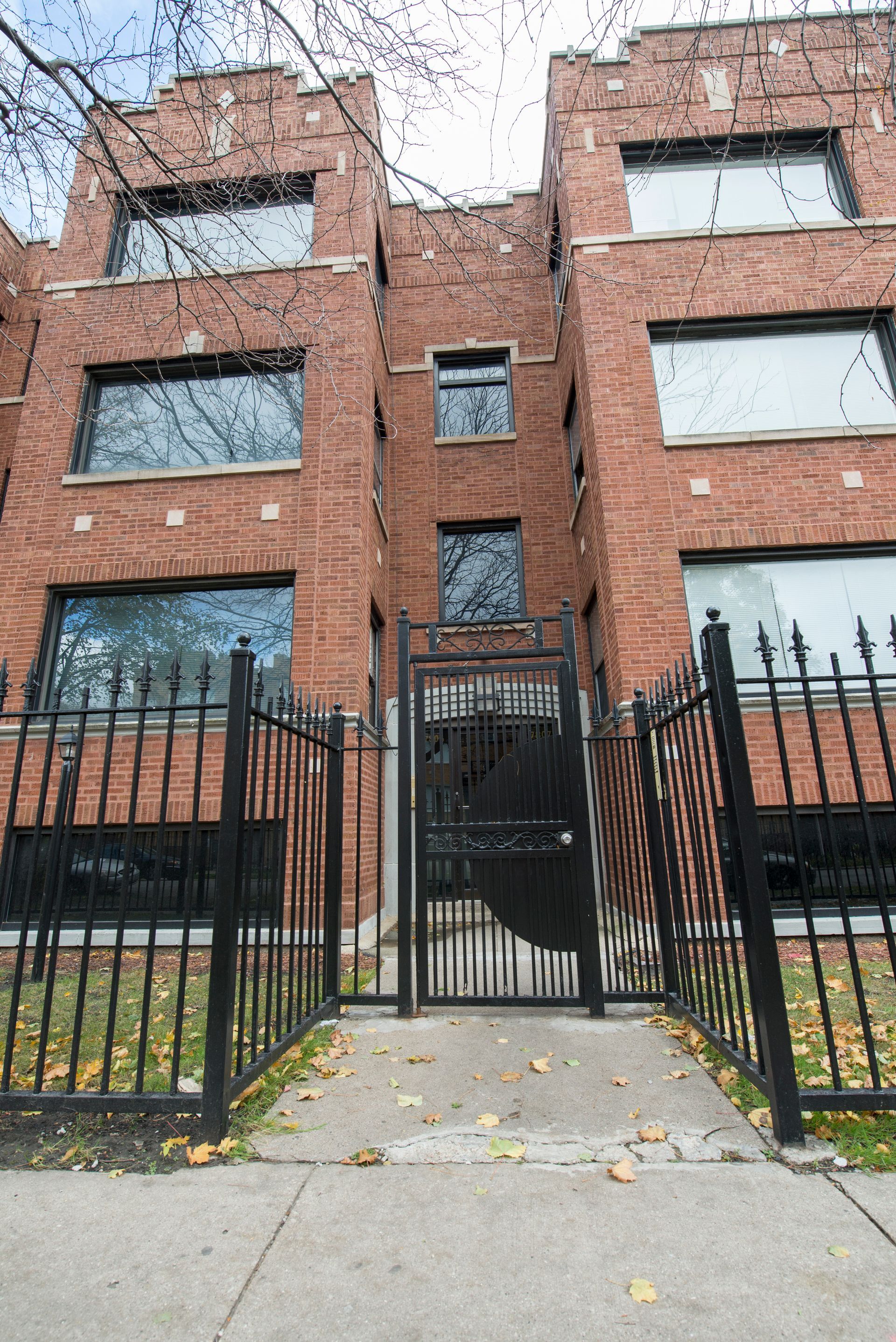 Brick row houses behind a black wrought iron fence. A walkway leads to a closed black gate.