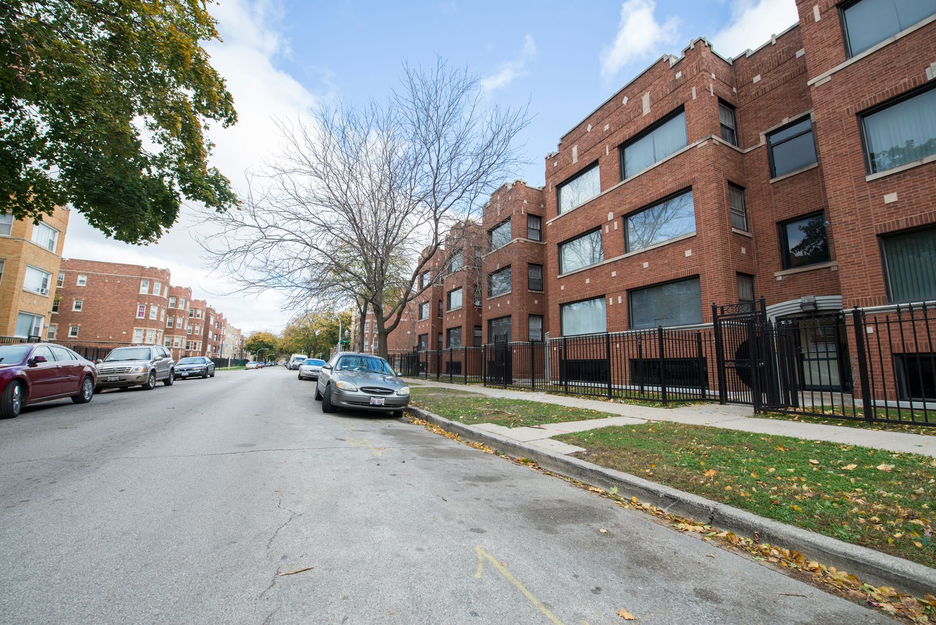Street with parked cars and brick apartment buildings on a sunny day.
