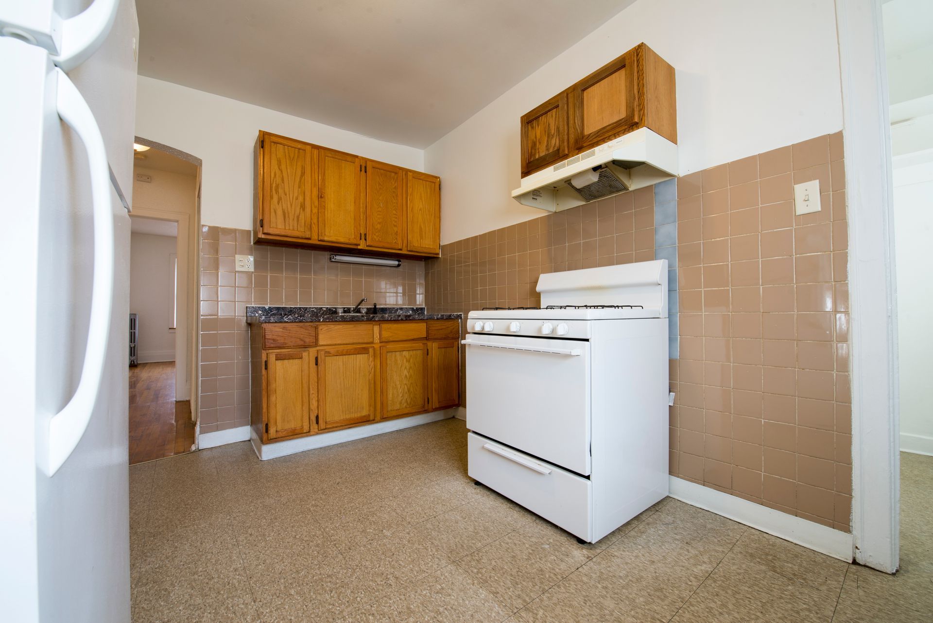 Kitchen with white appliances, wooden cabinets, and tan tile backsplash.