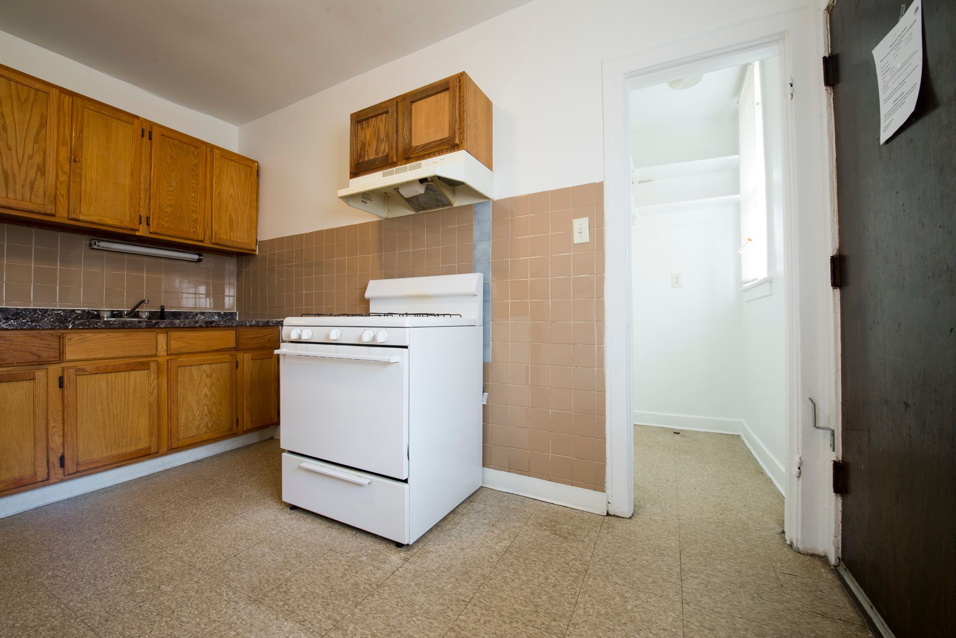 Kitchen with white appliances, wooden cabinets, and a doorway to a small room.