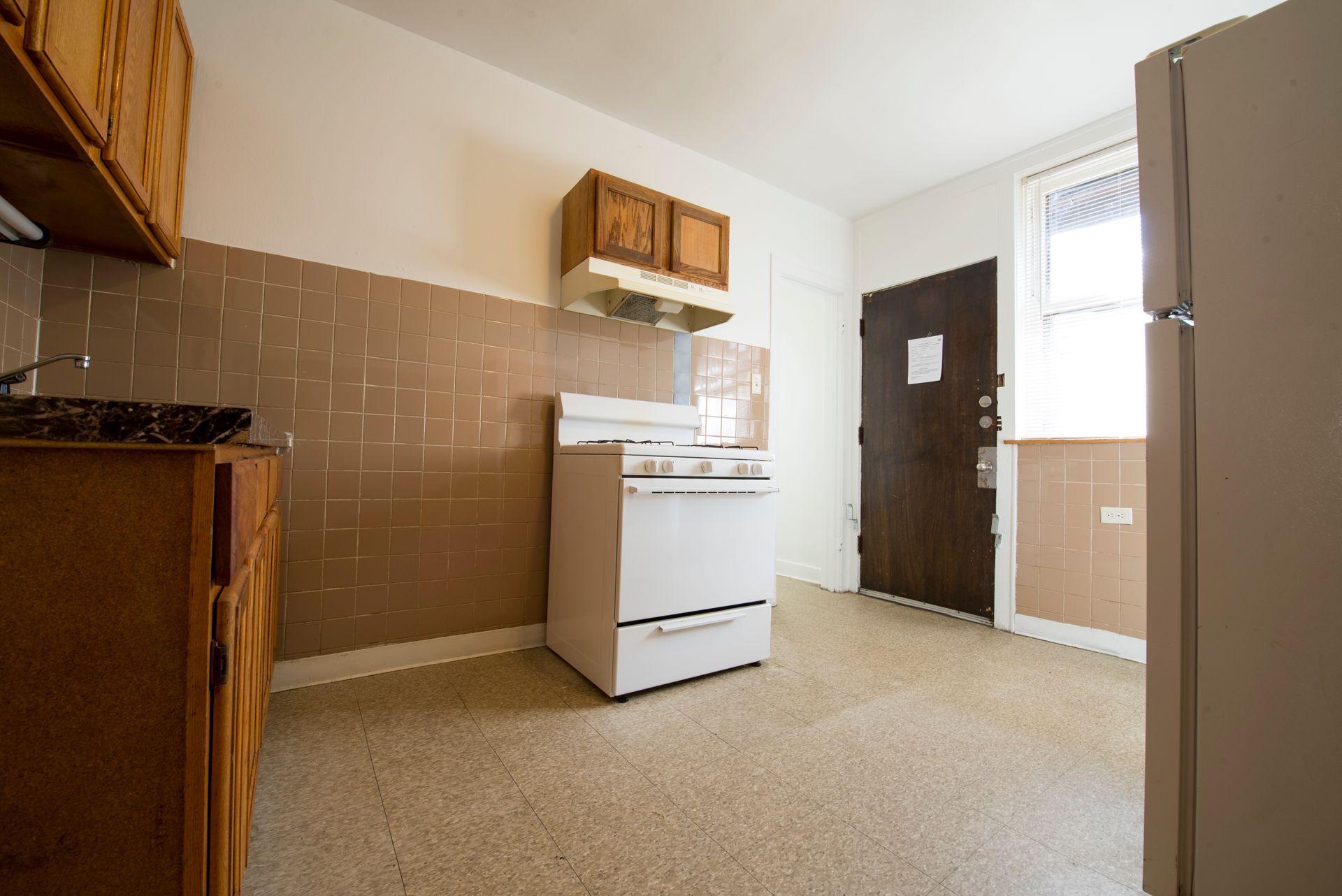 Empty kitchen with brown cabinets, stove, and tile backsplash.