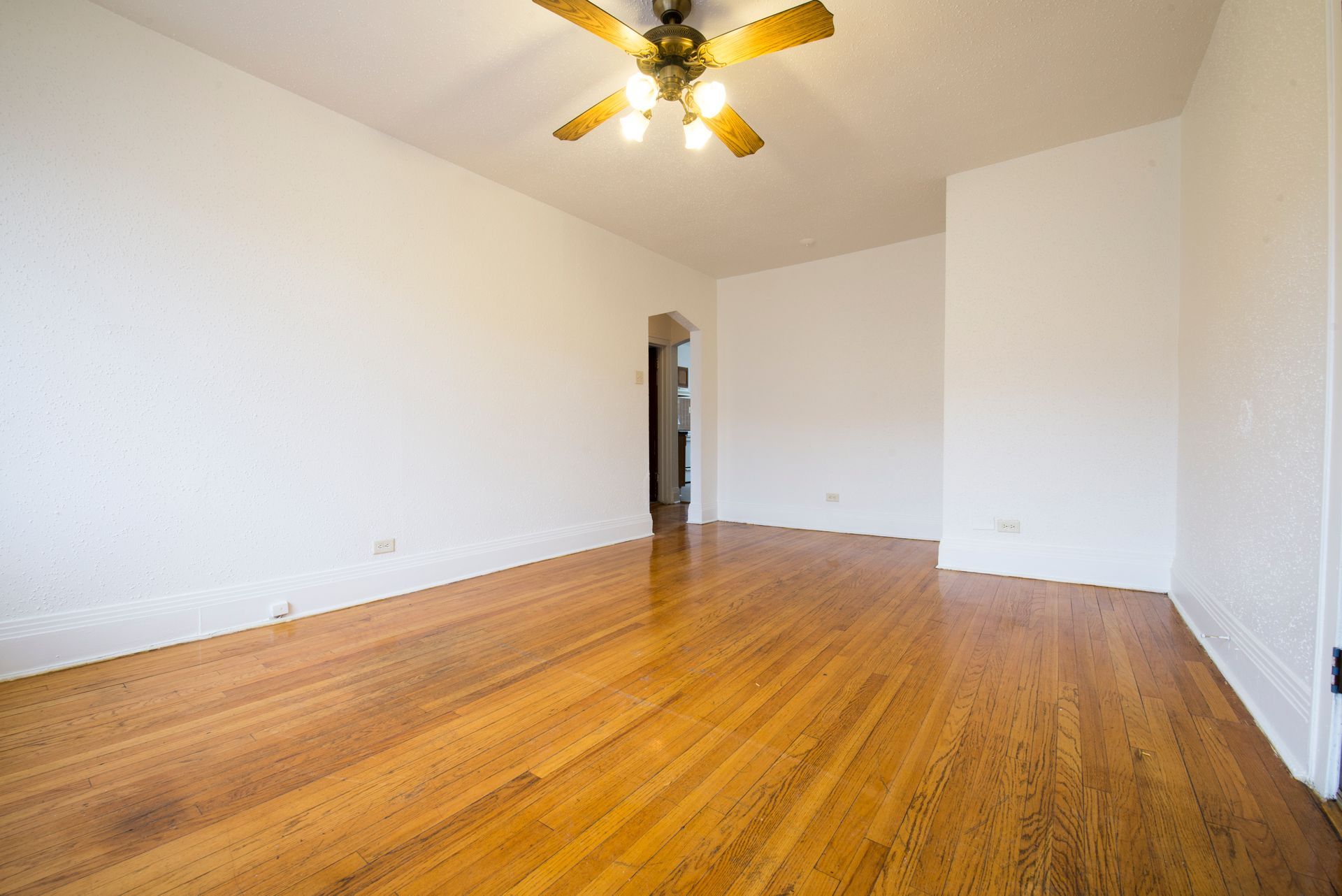 Empty room with hardwood floors, white walls, and a ceiling fan.