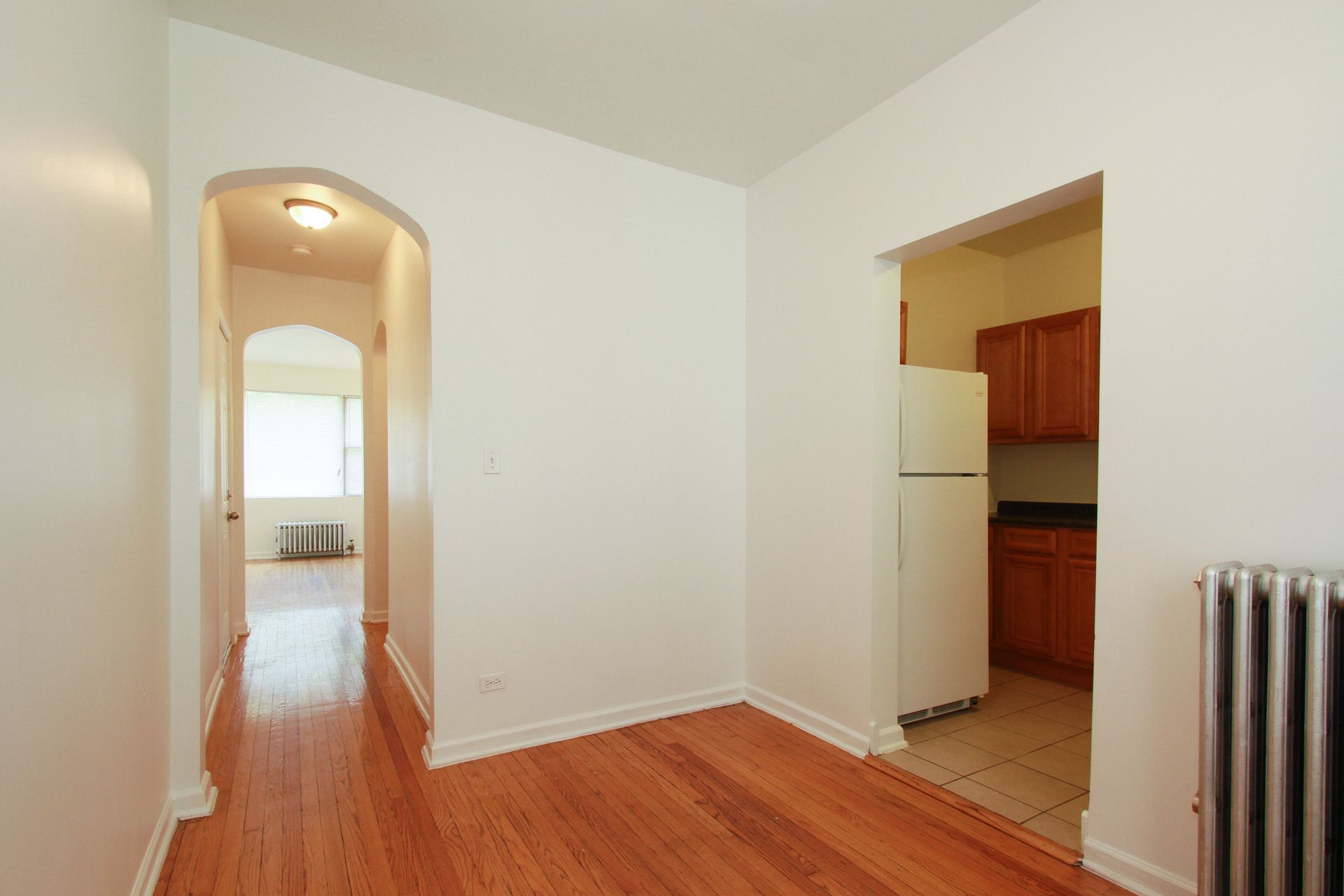 Interior of an apartment with hardwood floors, a hallway, and a kitchen visible.