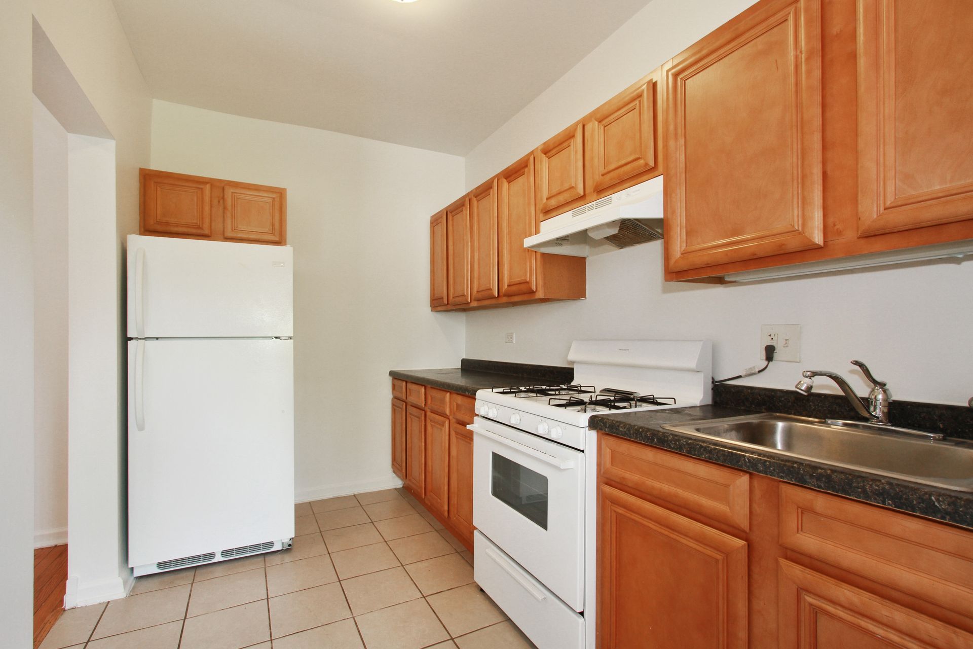 Kitchen with white appliances, brown cabinets, dark countertops, and tile flooring.