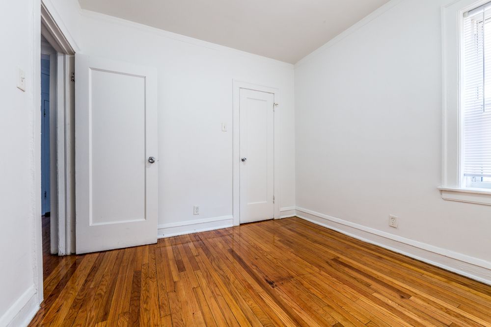 Empty room with wood floor, white walls, two doors, and a window.