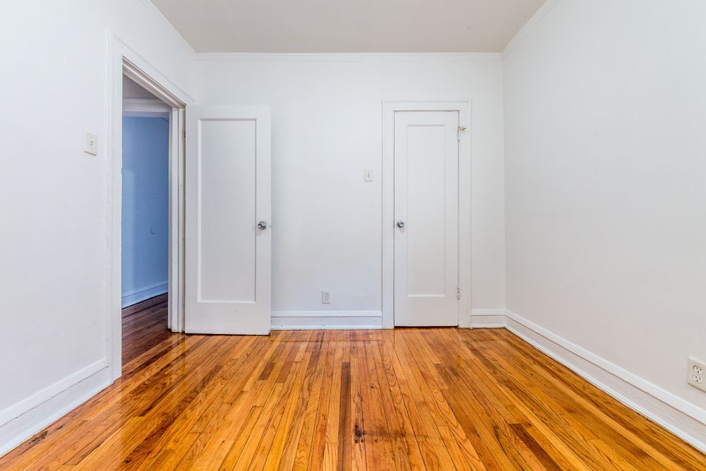 Empty room with hardwood floor, white walls, and two closed doors.