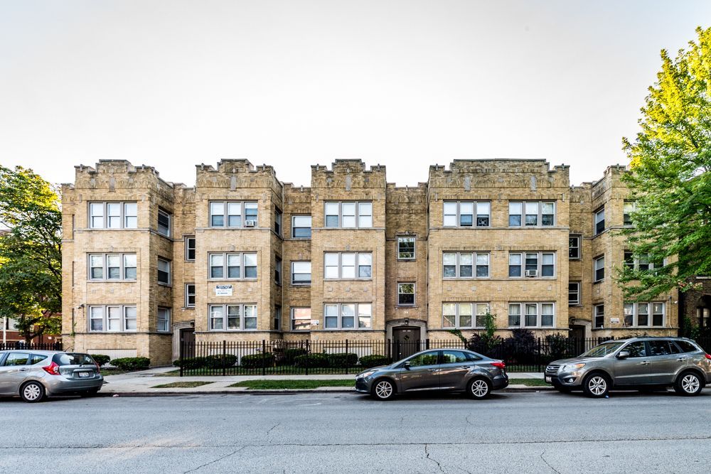 Multi-story brick apartment building with cars parked on the street in front.