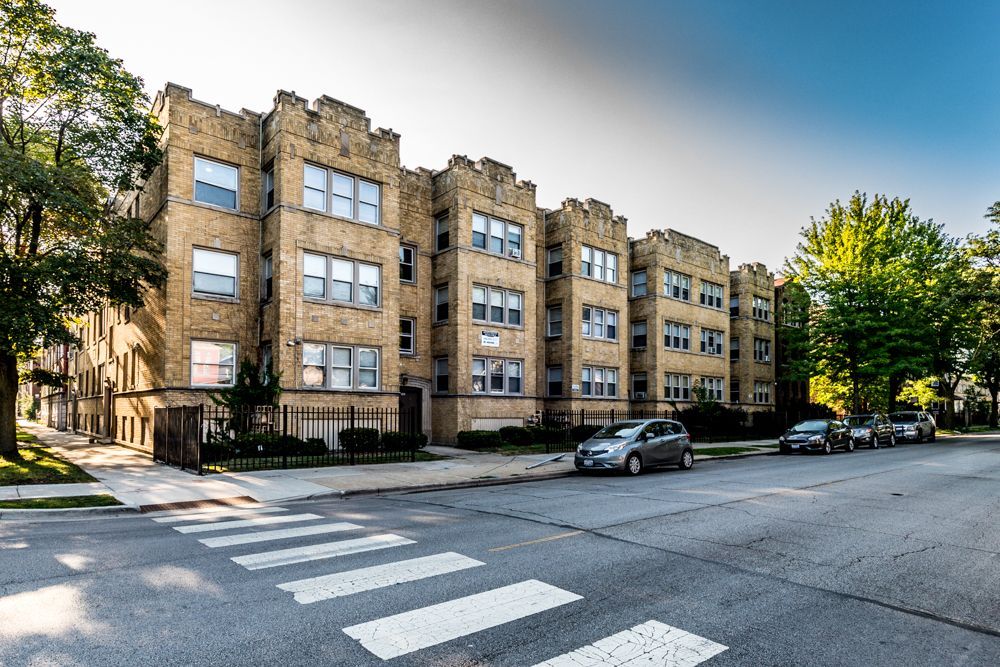 Apartment building with beige brick facade, cars parked on street, crosswalk.