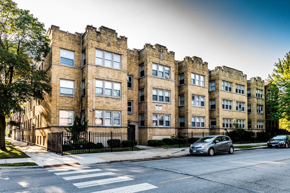 Multi-story brick apartment building on a city street; cars parked in front.