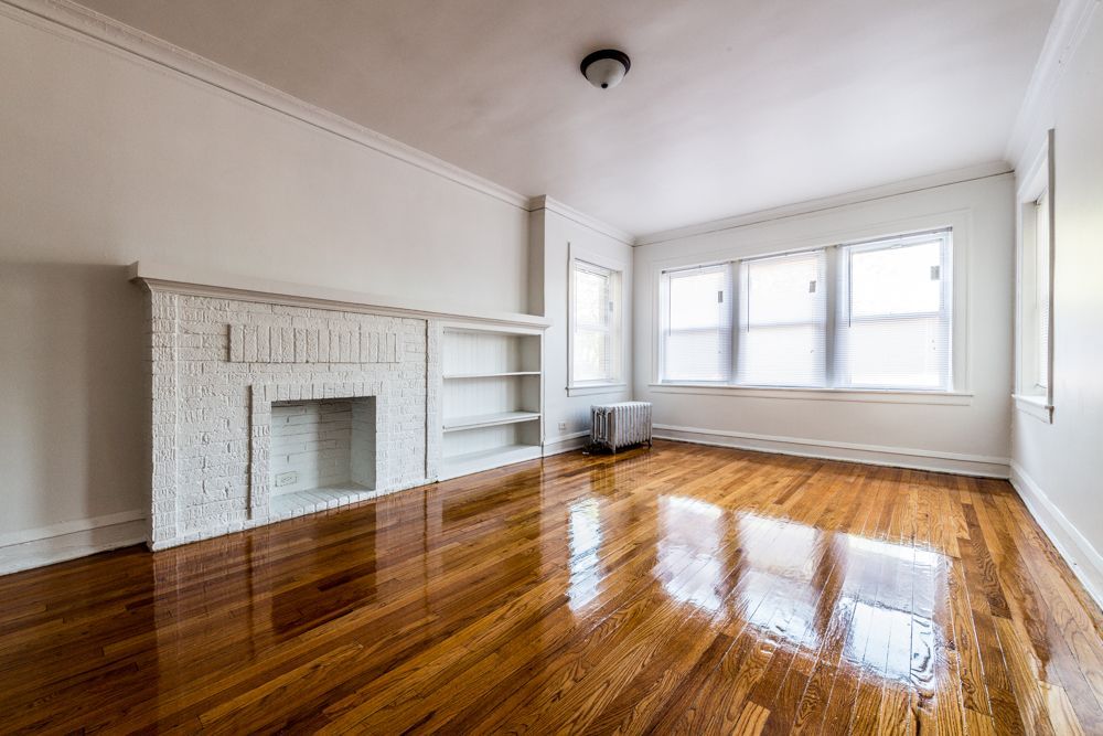 Empty room with polished wood floor, fireplace, and windows.