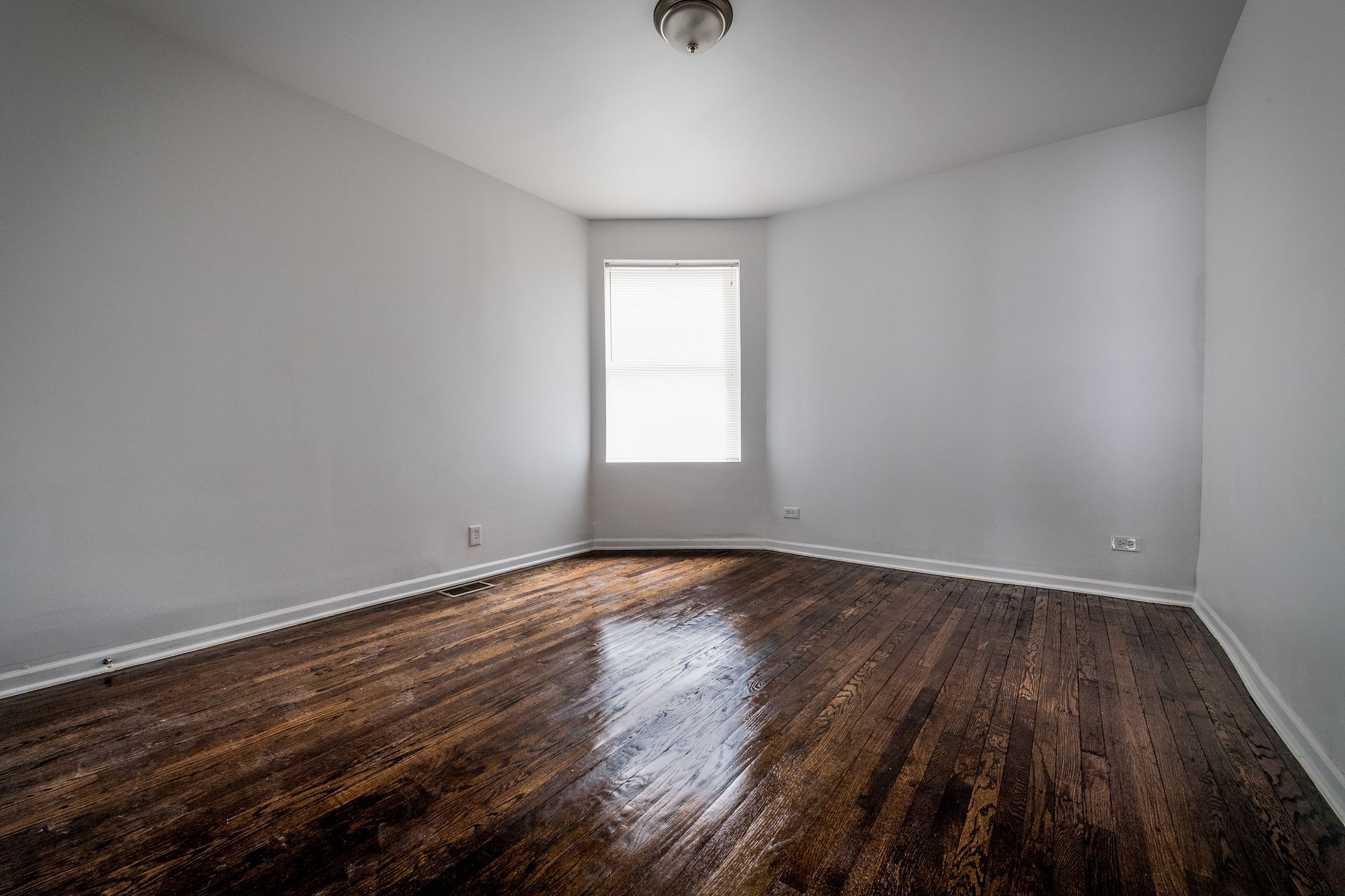 Empty room with glossy, dark wood floors and a window. White walls and trim.