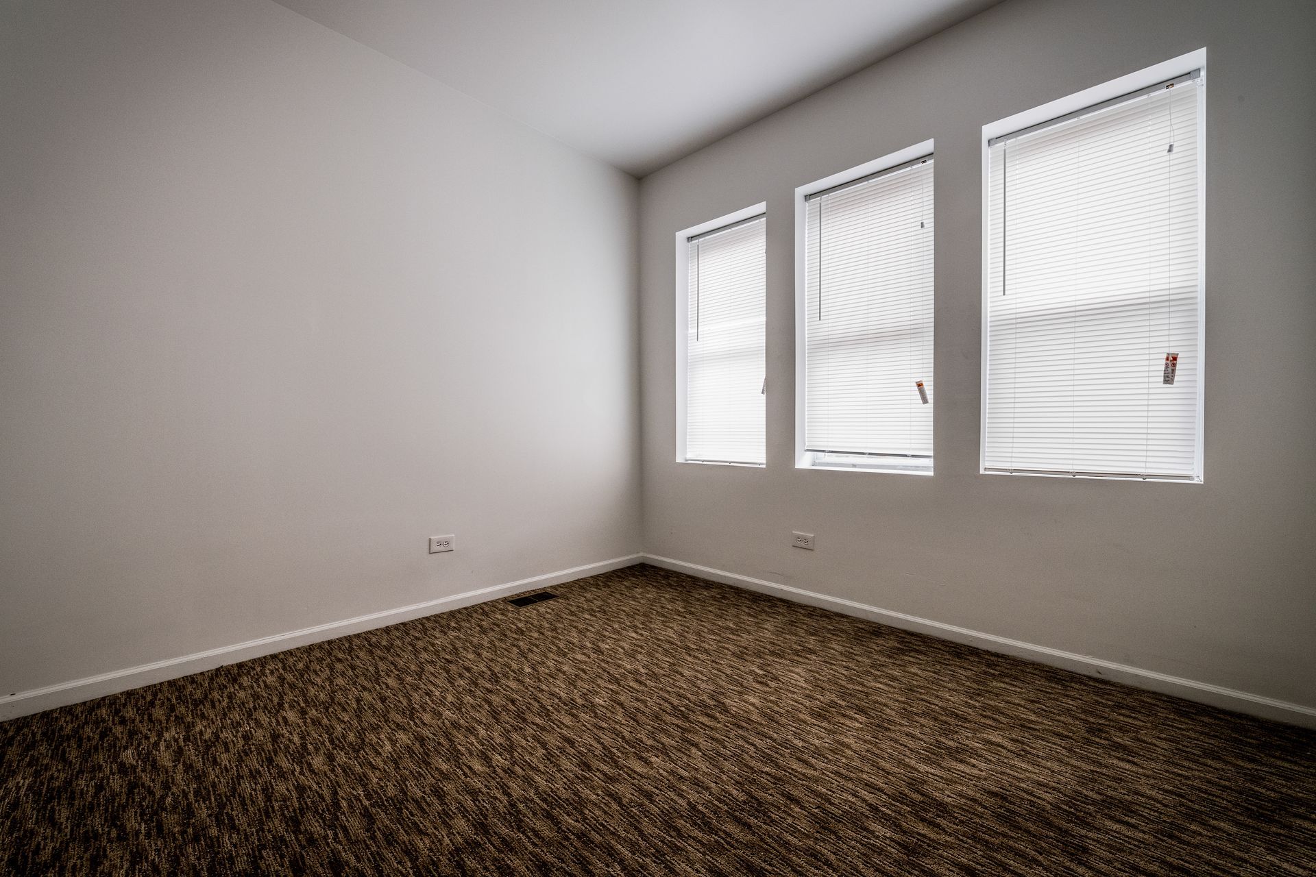 Empty room with brown carpet, three windows with blinds, and white walls.