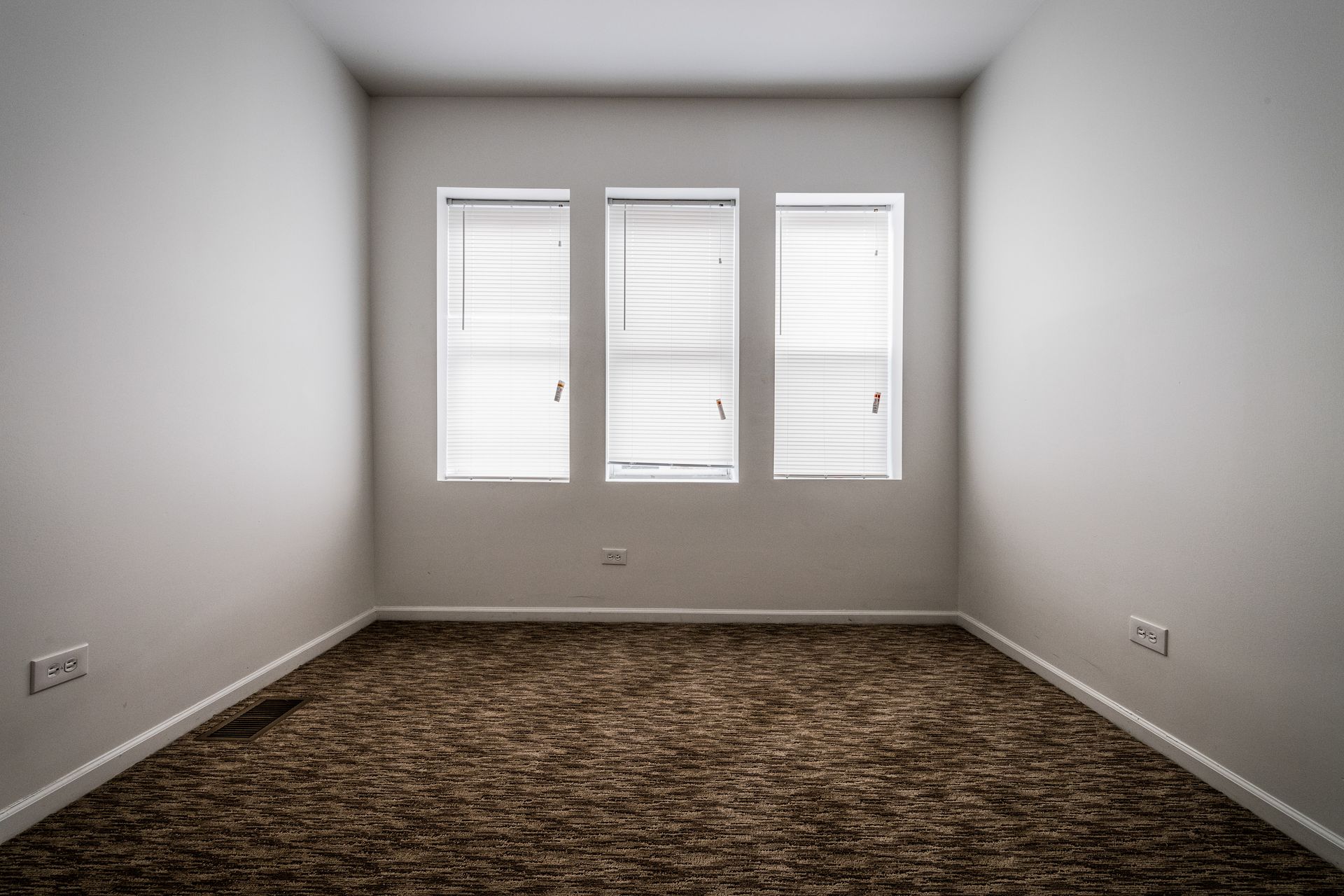 Empty room with three windows and brown carpet.