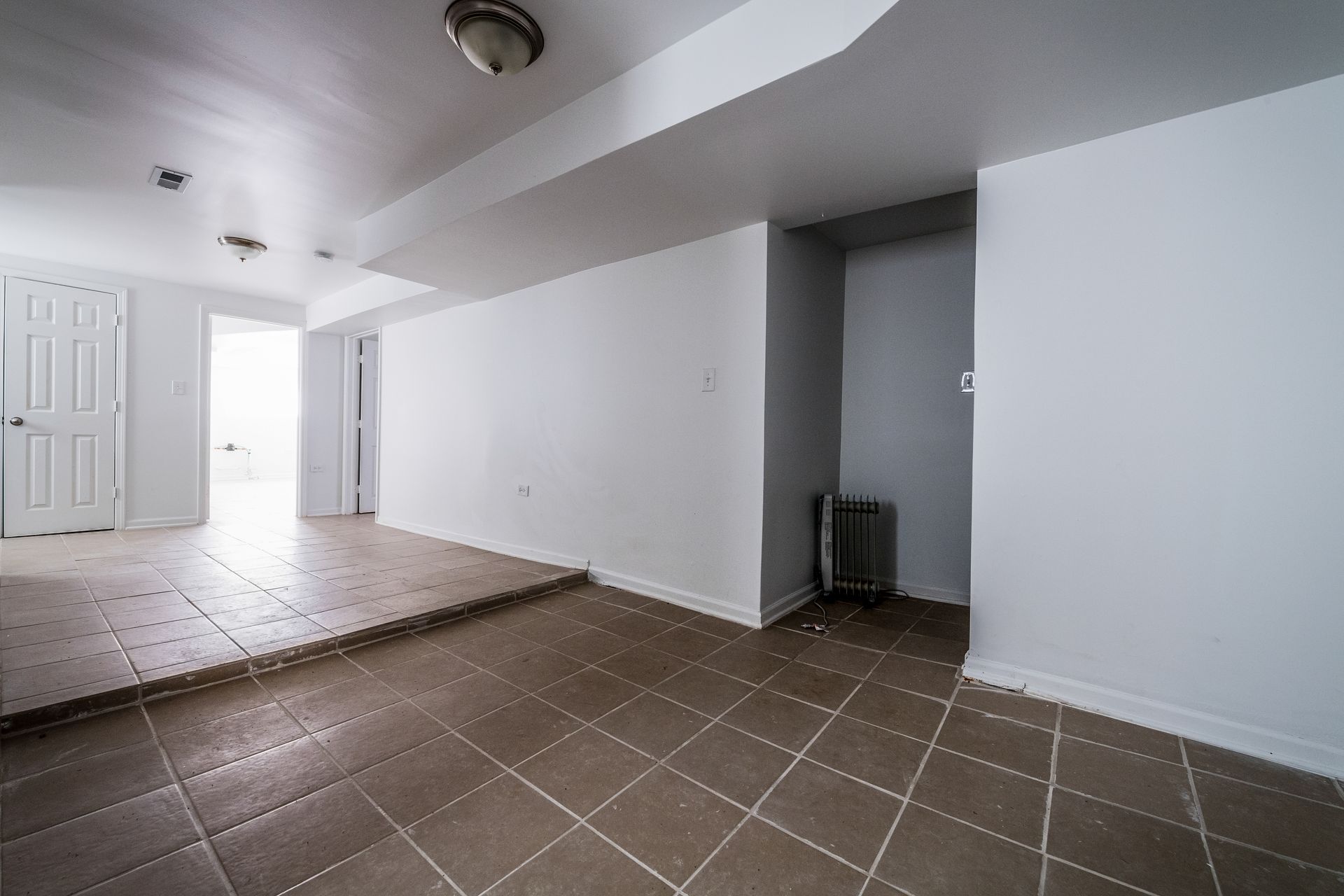 Empty room with tiled floor, white walls, and a raised section.