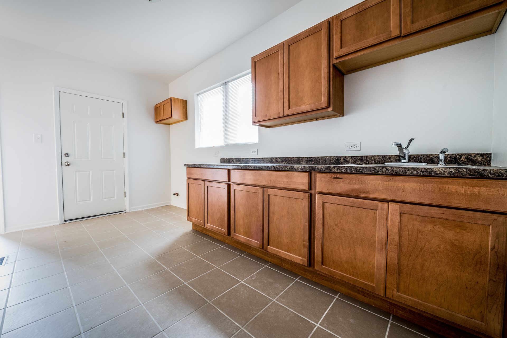 Empty kitchen with wooden cabinets, countertop, window, and tiled floor.