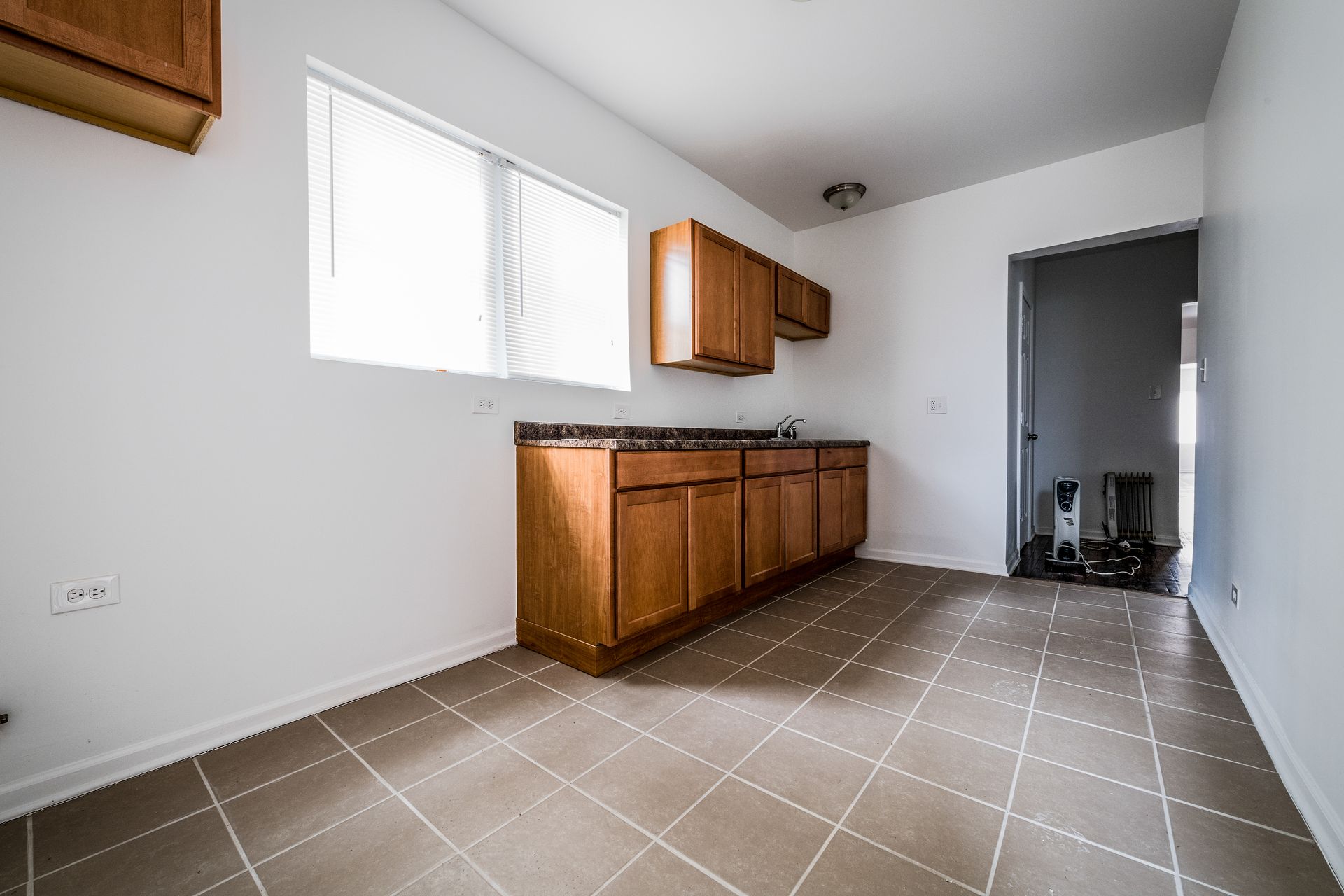 Empty kitchen with wood cabinets, countertop, window, and diamond-patterned tile floor.