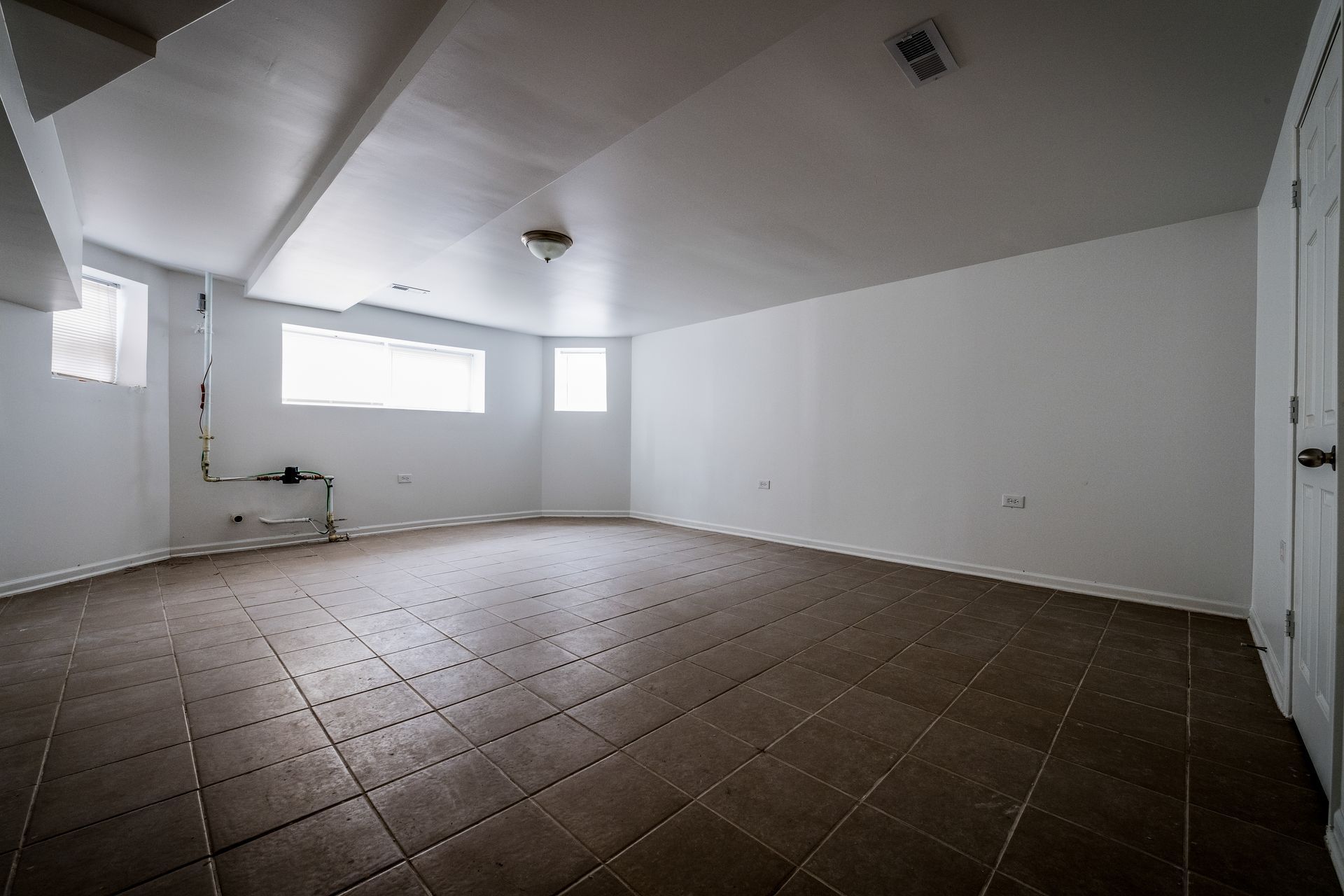 Empty, tiled-floor basement with white walls, three small windows, and a doorway on the right.