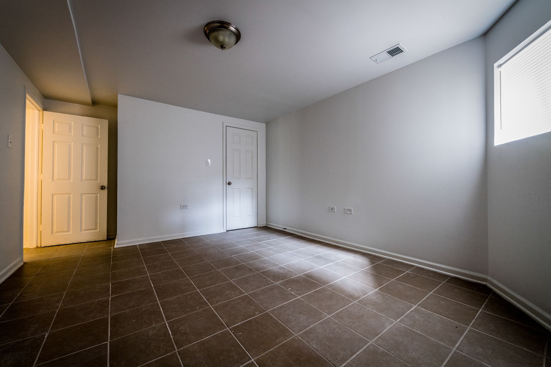 Empty room with dark tiled floor, white walls, two doors, and a small window.