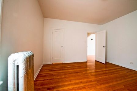 Empty room with hardwood floors, white walls, two doors, and a radiator.